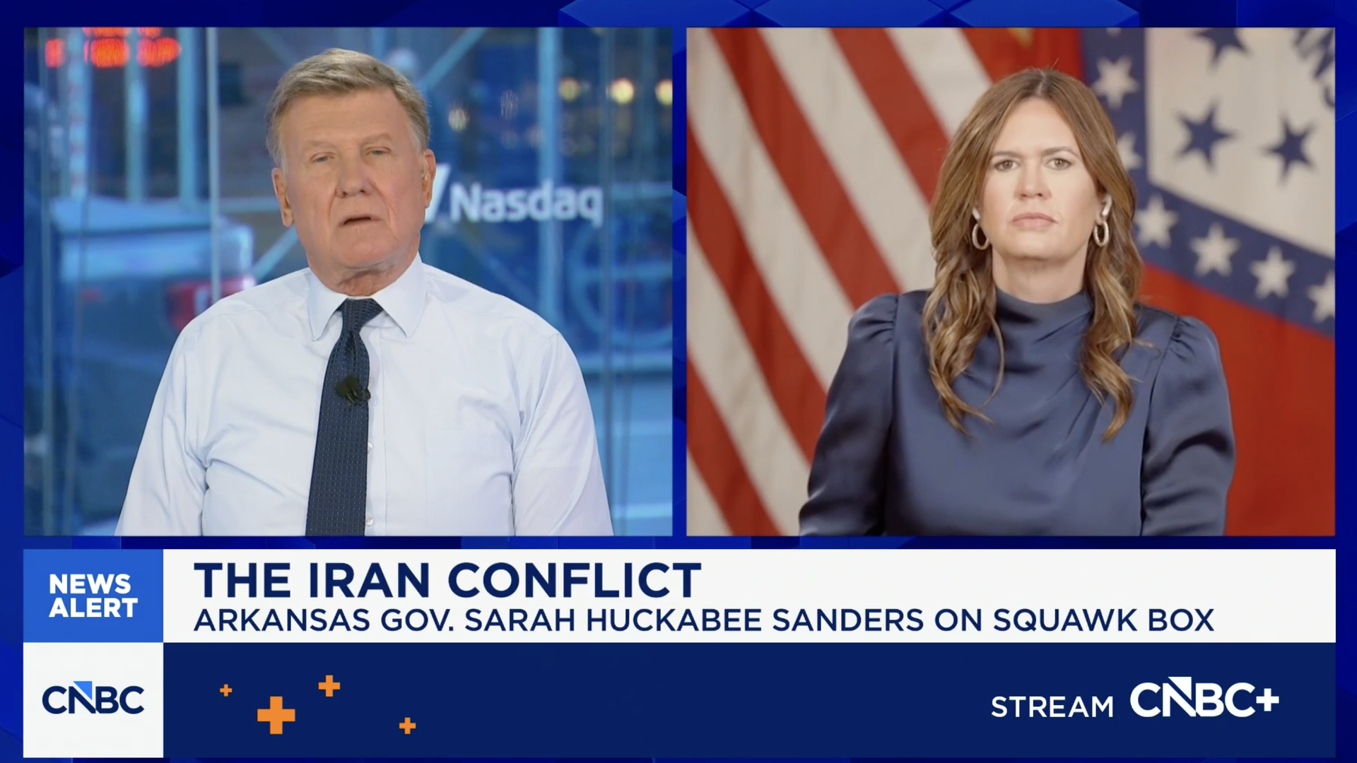 Split-screen TV interview: a male anchor on the left and Arkansas Gov. Sarah Huckabee Sanders on the right, with U.S. and Arkansas flags behind her and a headline about the Iran conflict.