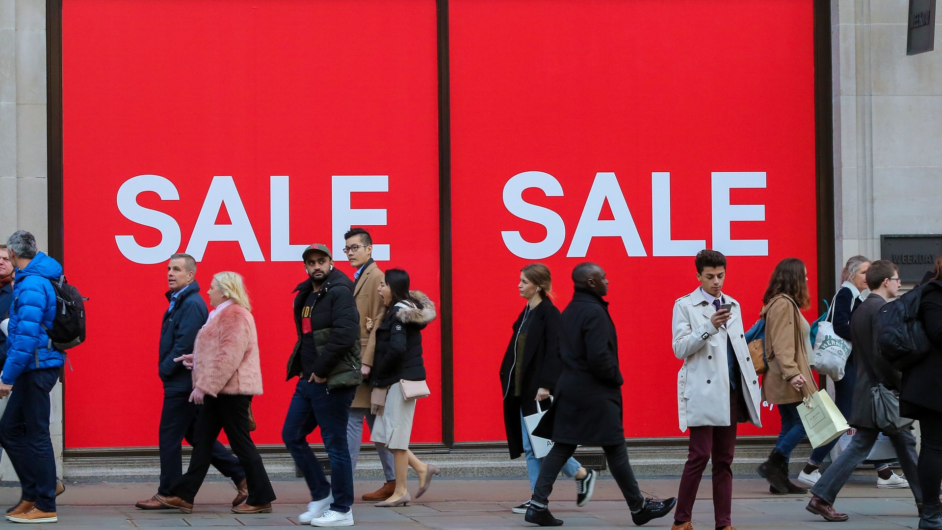 Sale sign on wall as shoppers walk by.