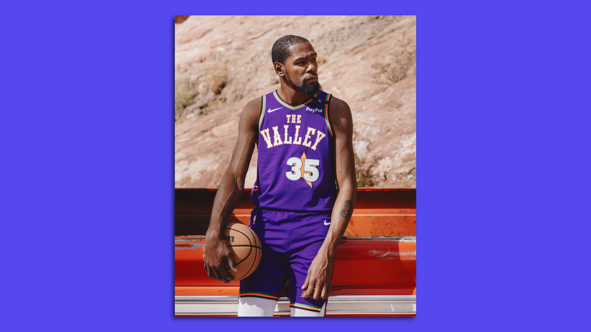 Kevin Durant leans against the side of a pickup truck wearing his Phoenix Suns uniform and holding a basketball in the desert.