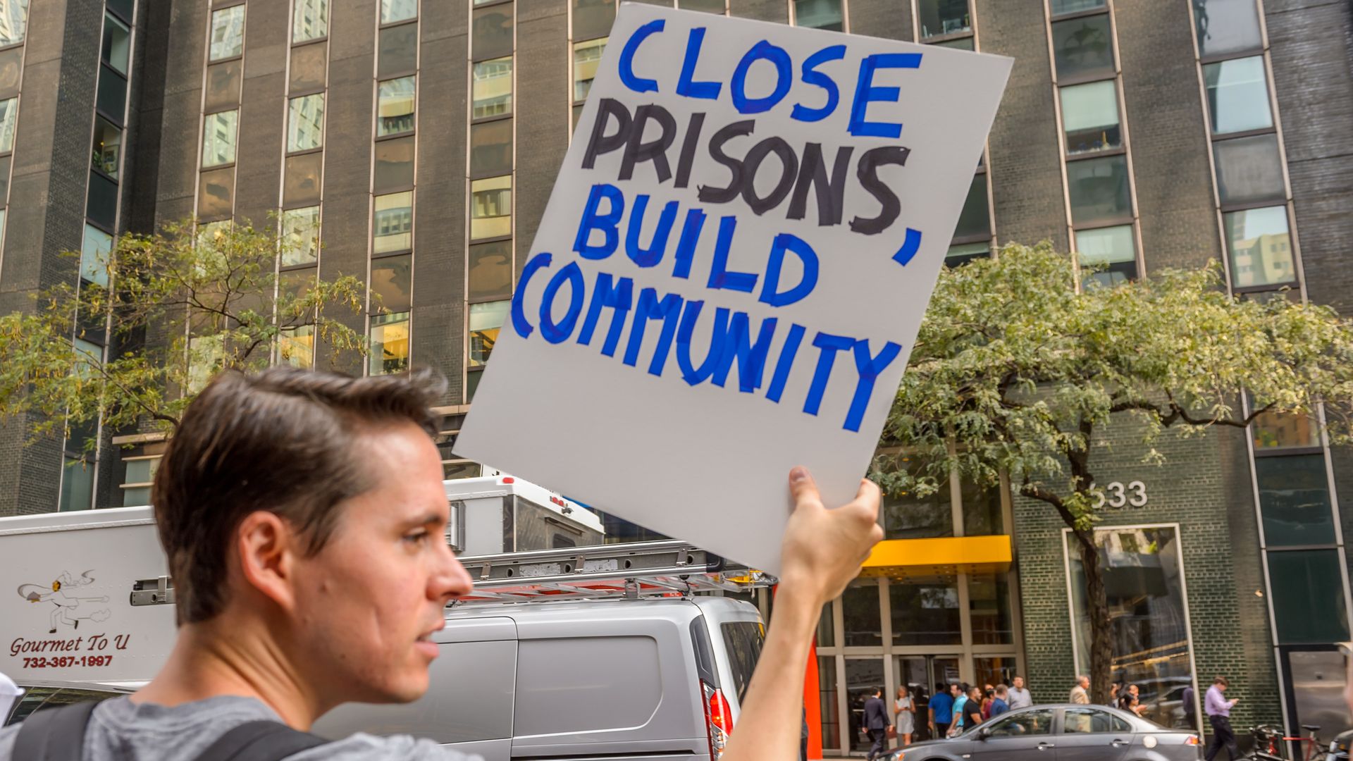 Photo of a person holding a sign that says "Close prisons, build community"