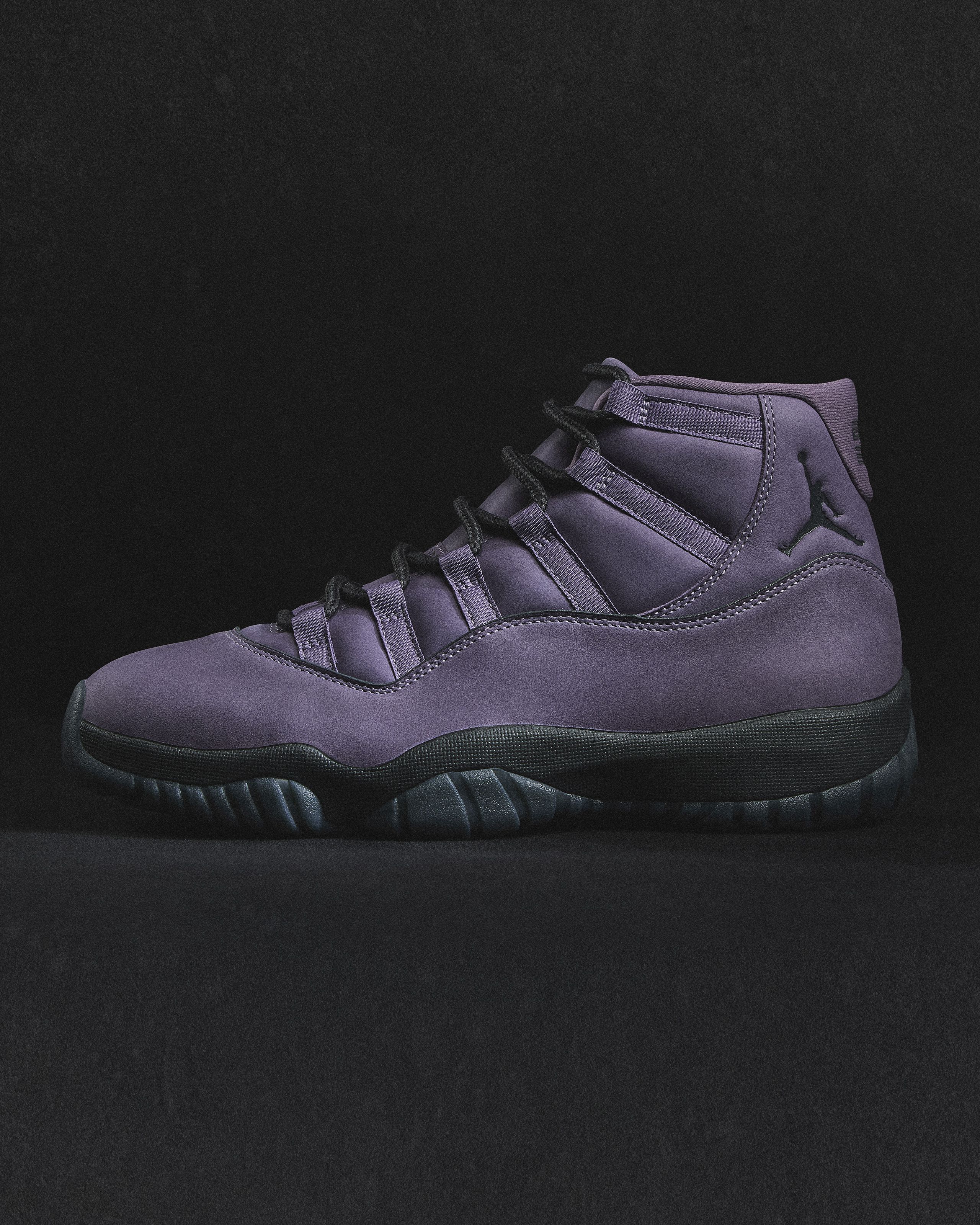 Side view of a high-top purple Air Jordan sneaker with black laces and a black sole against a dark background, featuring the Jumpman logo near the heel.