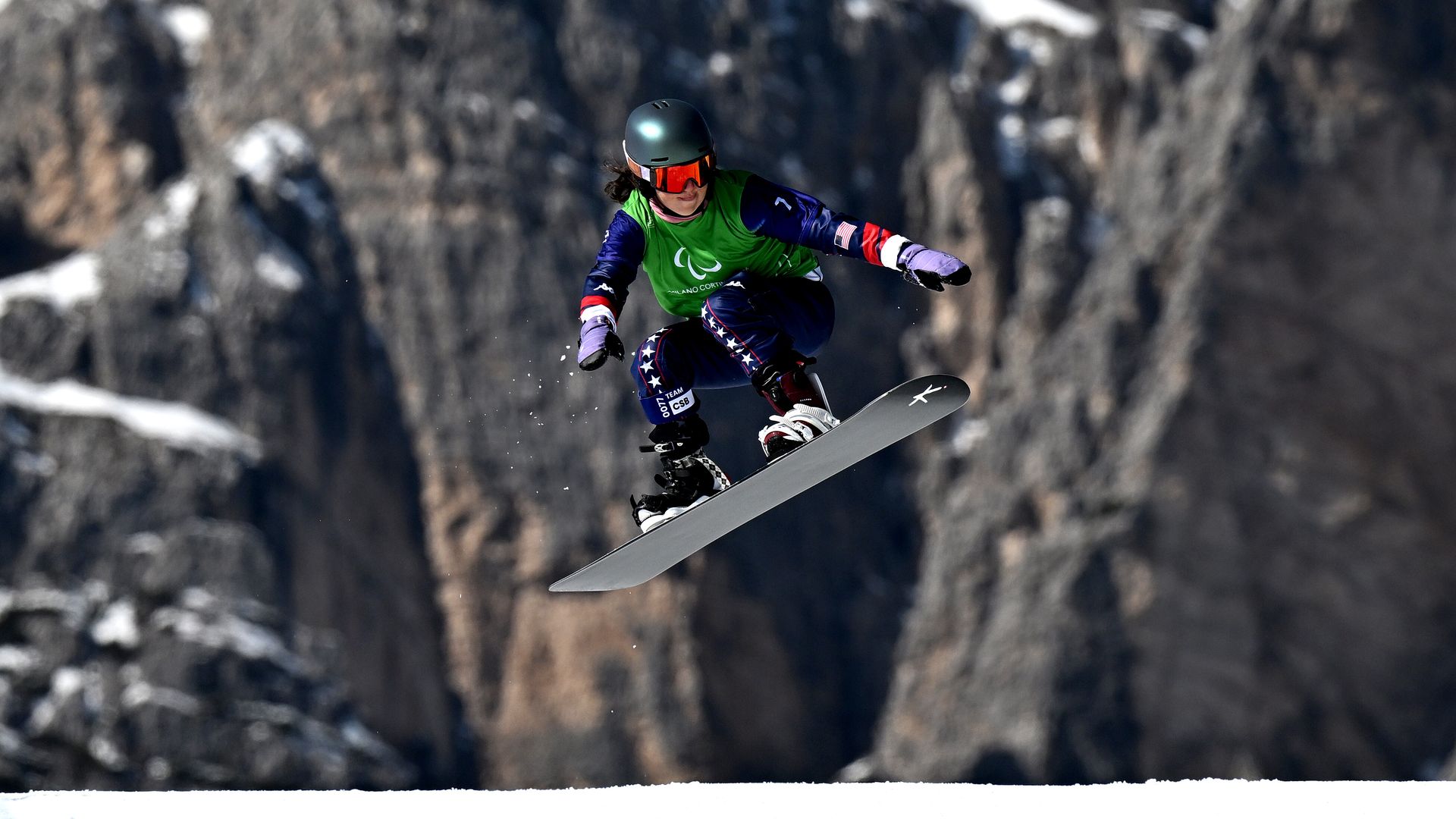 A Team USA Paralympic snowboarder Kate Delson rides in the air with mountains 