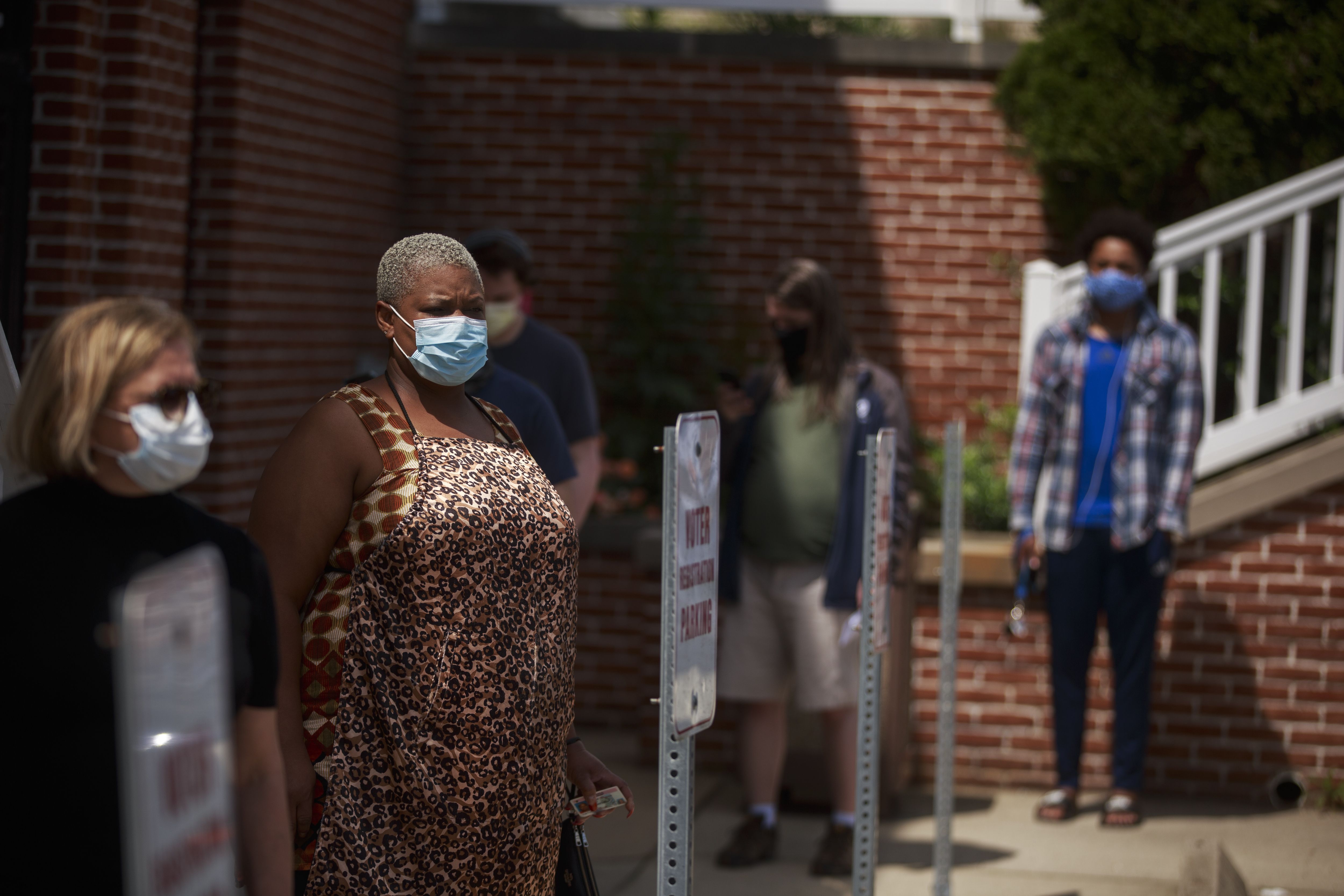 Two women stand at the front of a line ofpeople wearing face masks and standing outside