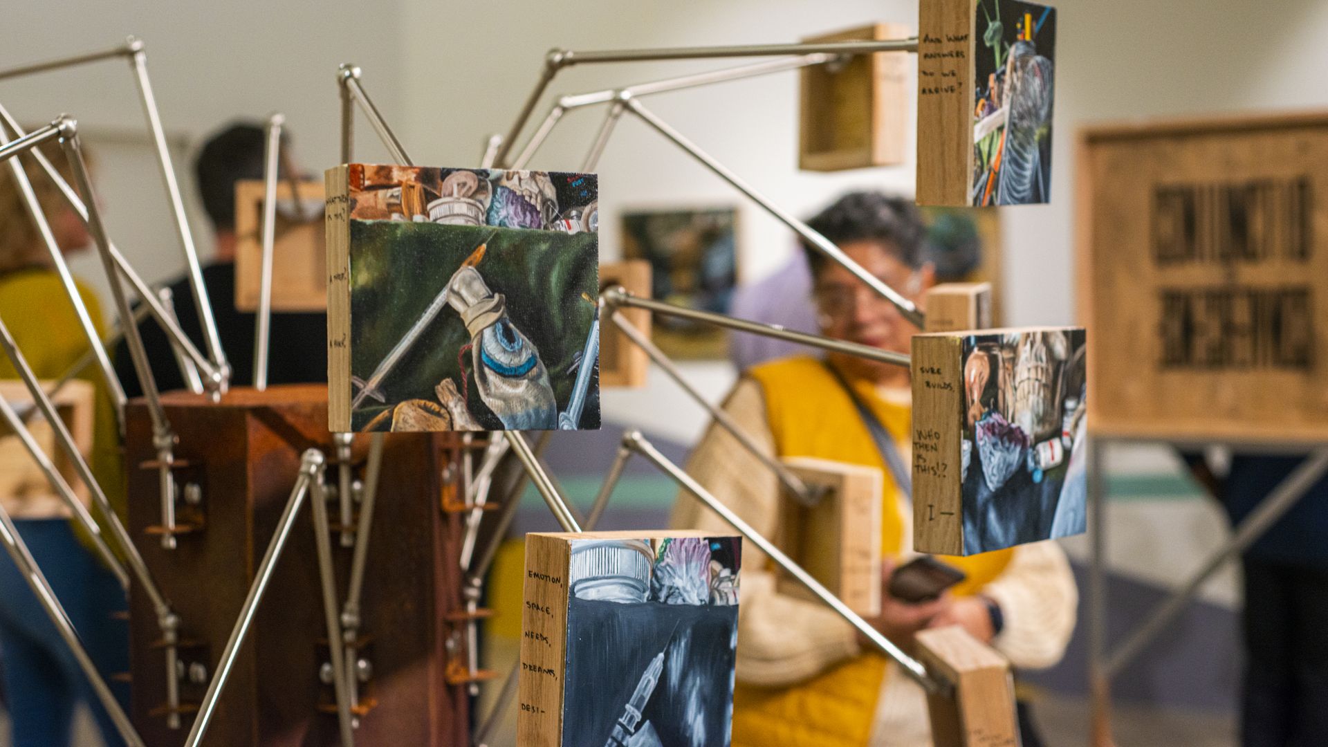 A spider-like sculpture with metal arms has pieces of paintings attached to each arm.