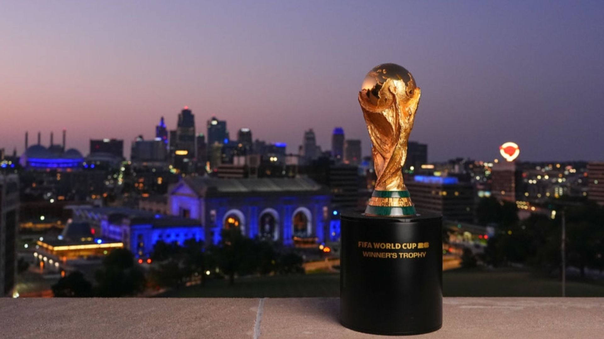 The FIFA World Cup Trophy is displayed at National WWI Museum and Memorial with the Kansas City skyline lit up blue in the background at night.