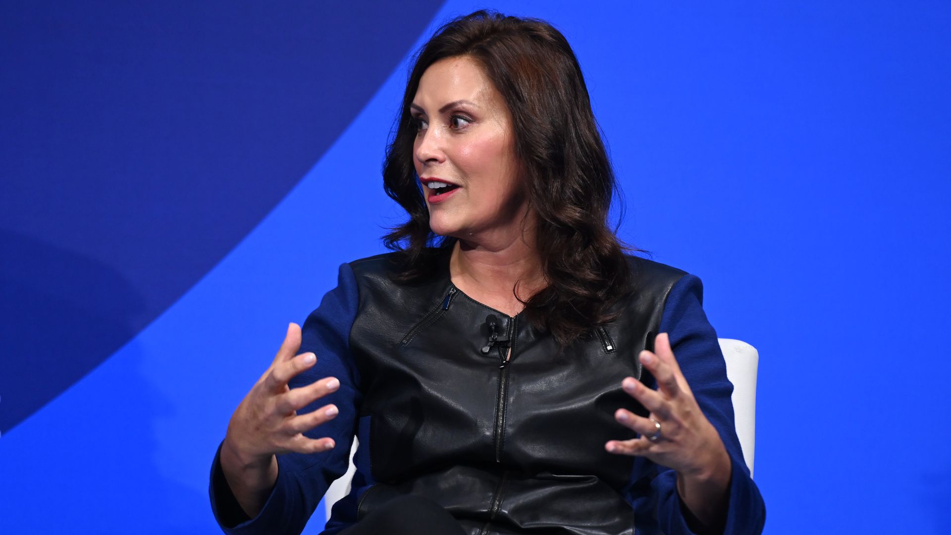 Wearing black, Gretchen Whitmer speaks while sitting at a white chair