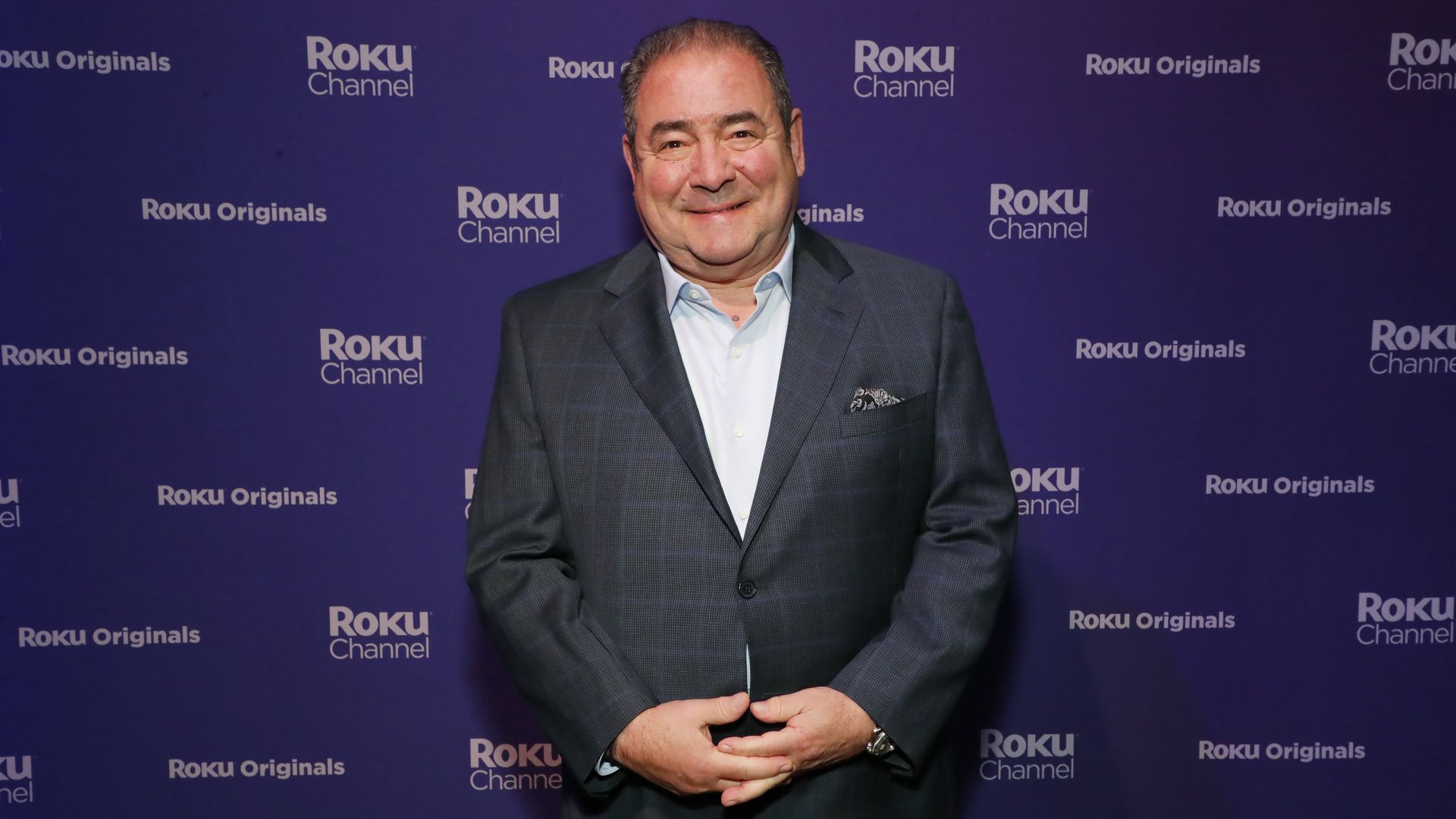 Image shows Emeril in a suit and smiling in front of a Roku backdrop.