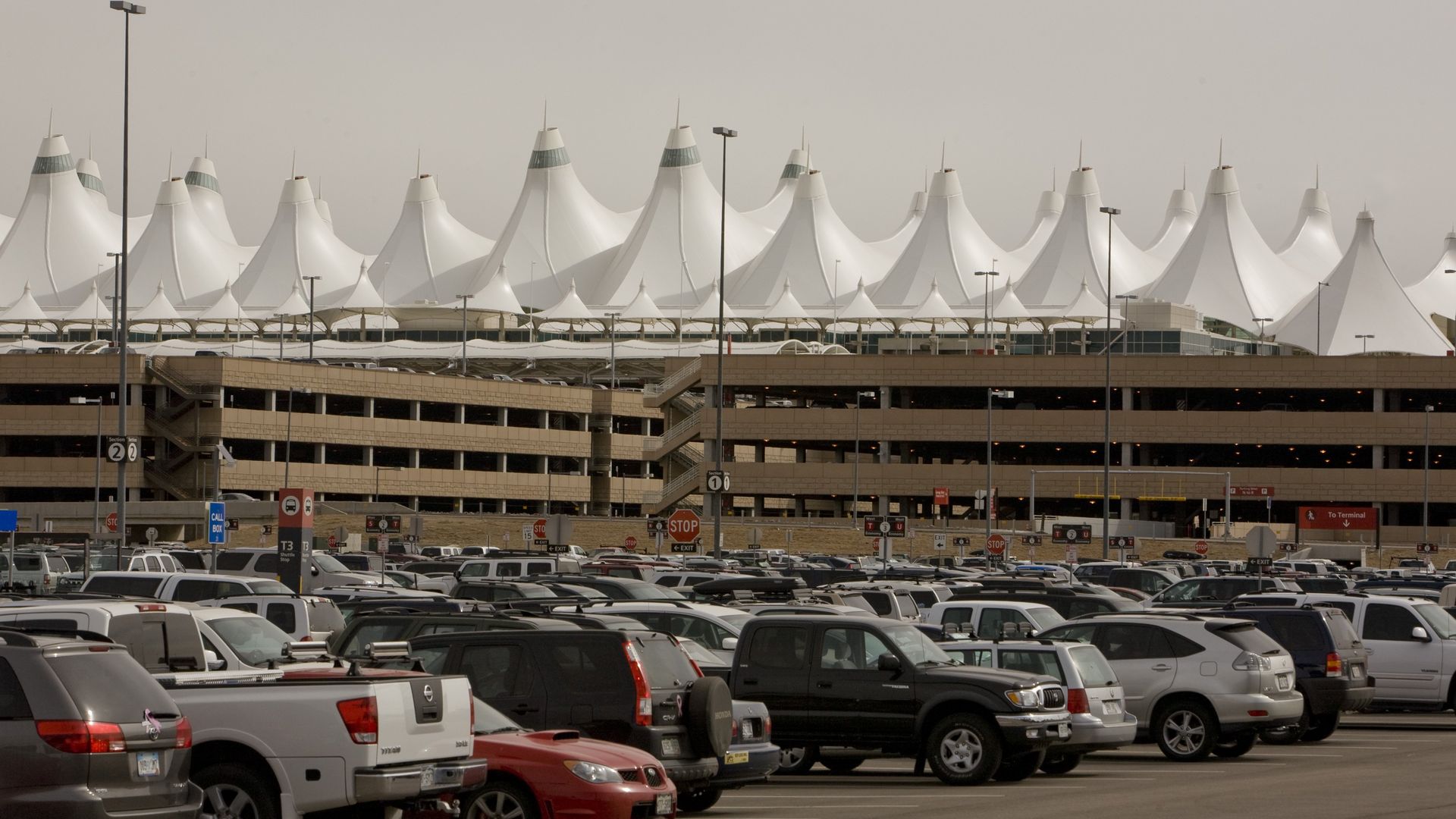 A photo of cars parked in a parking lot of Denver's airport, with the airport's signature white tents pictured in the background.
