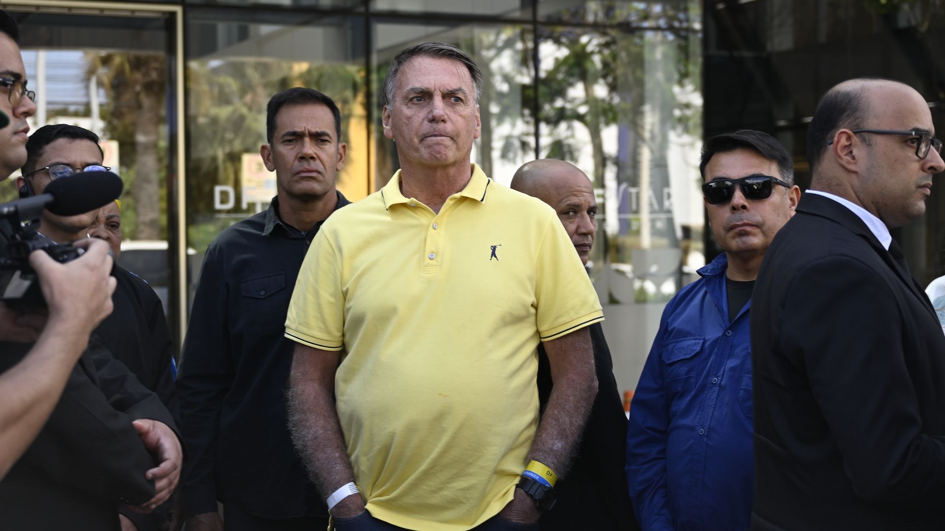 Jair Bolsonaro wears a yellow short-sleeved shirt as he places his hands in his pockets.