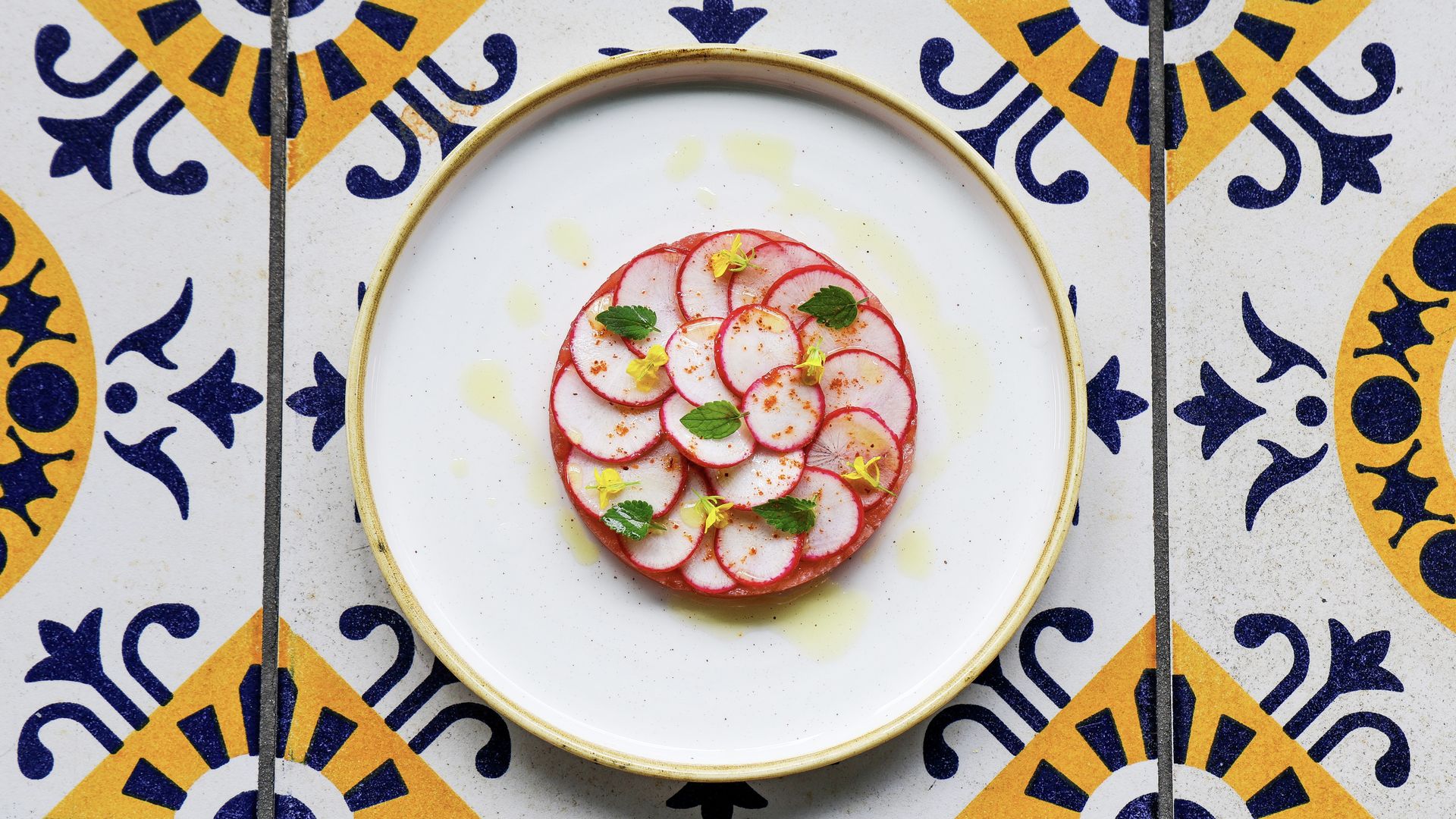 A tartare with radishes on top on a blue and white tile table