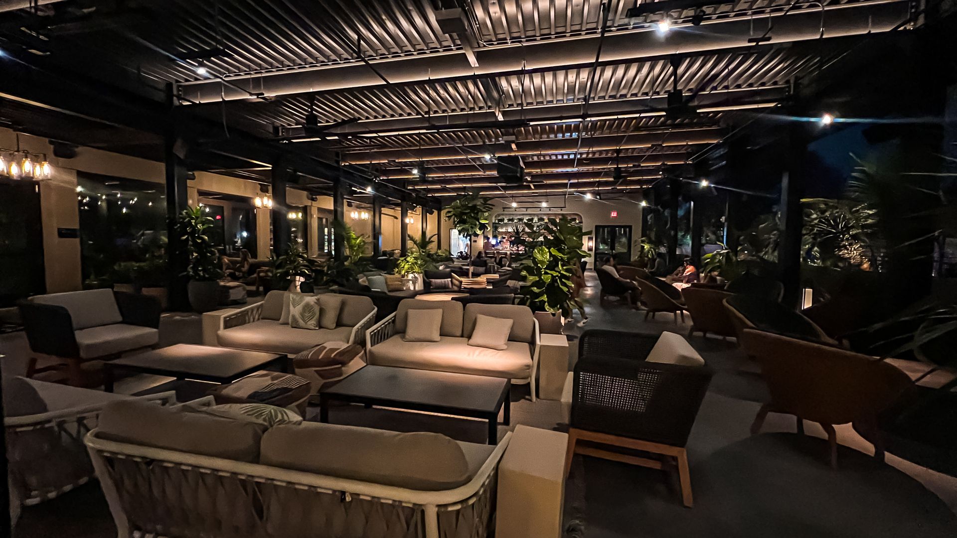 A dimly lit outdoor bar with multiple groups of lounge seating. 
