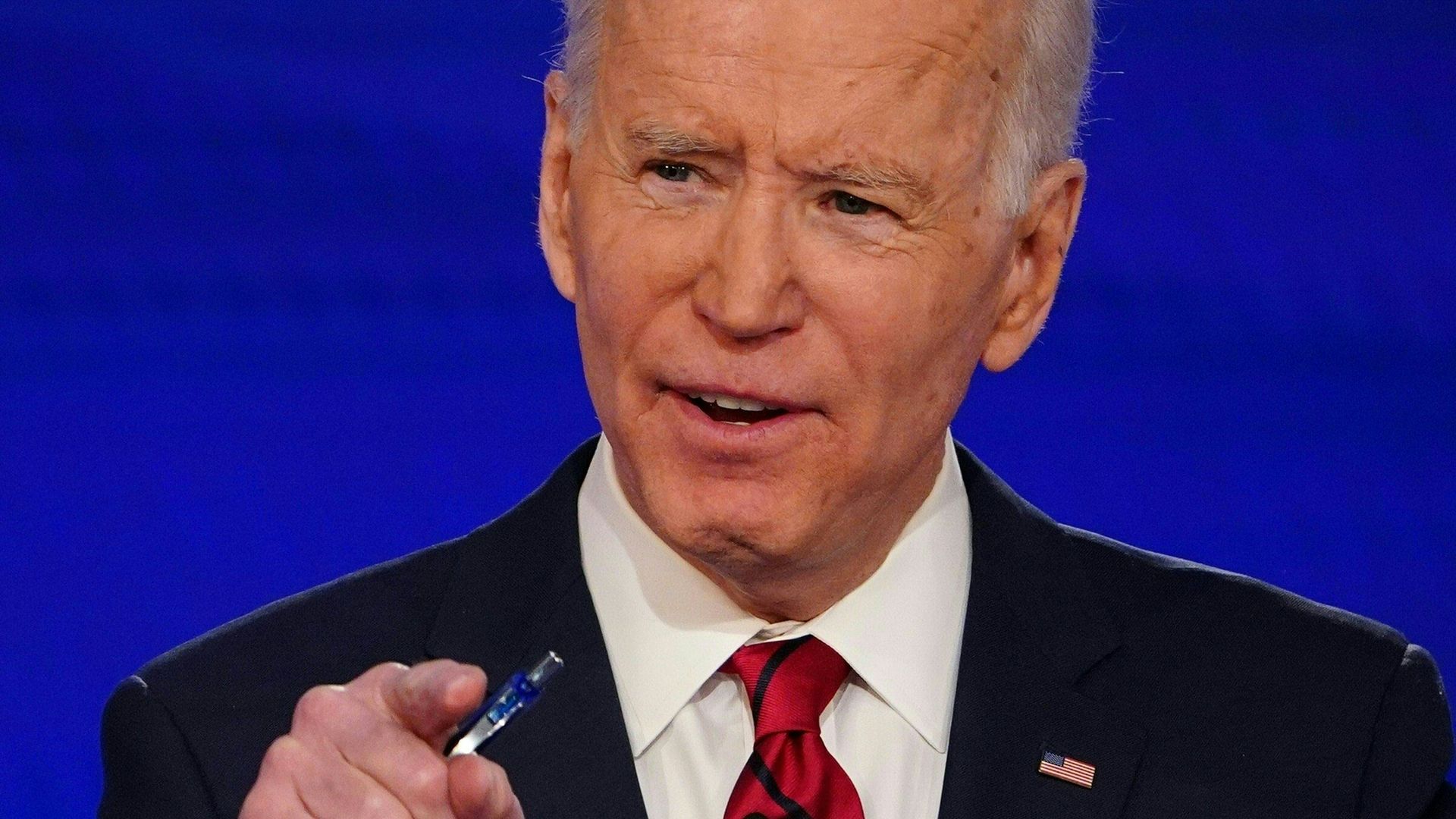 In this image, Joe Biden talks and holds a pen