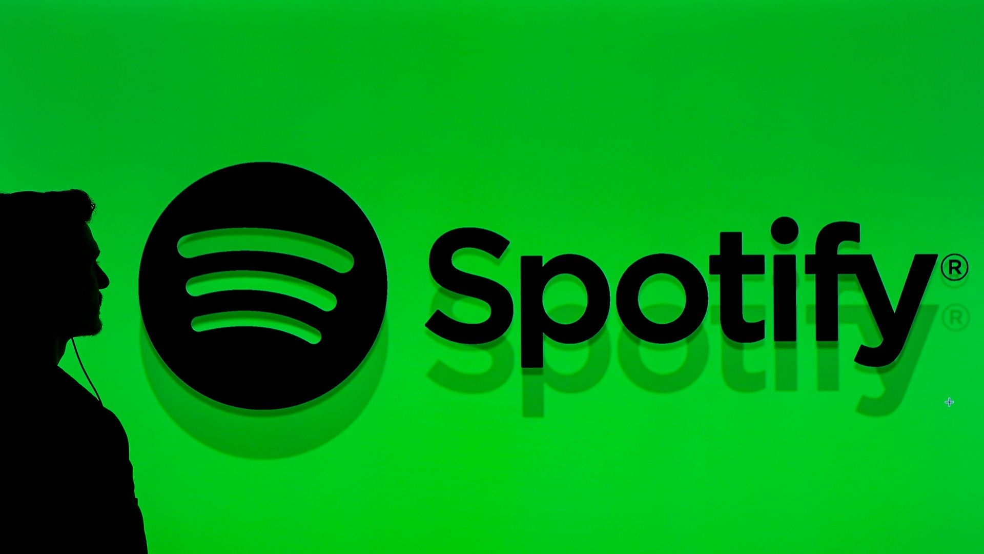 Silhouette of a person wearing earphones next to a large black Spotify logo on a bright green background.