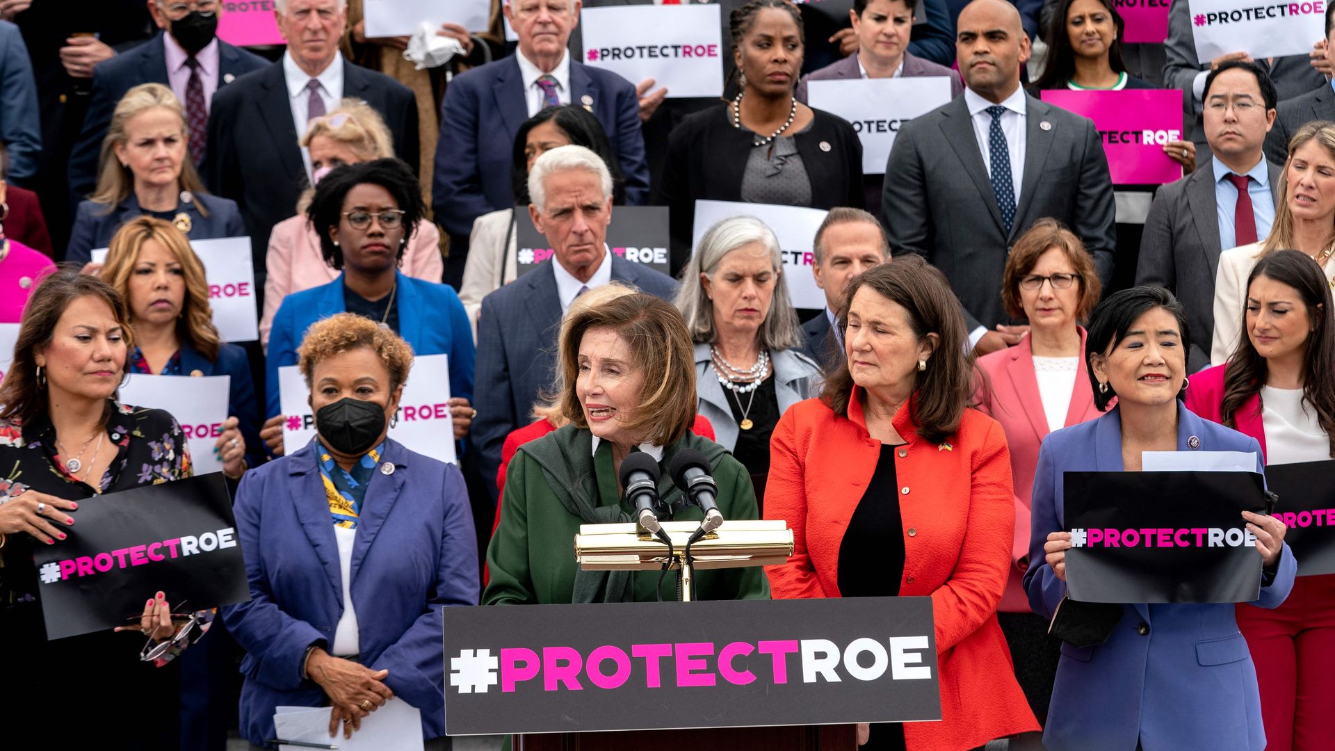 Photo of Nancy Pelosi speaking from a podium with a sign that says "#ProtectRoe" as other Congress members stand behind her