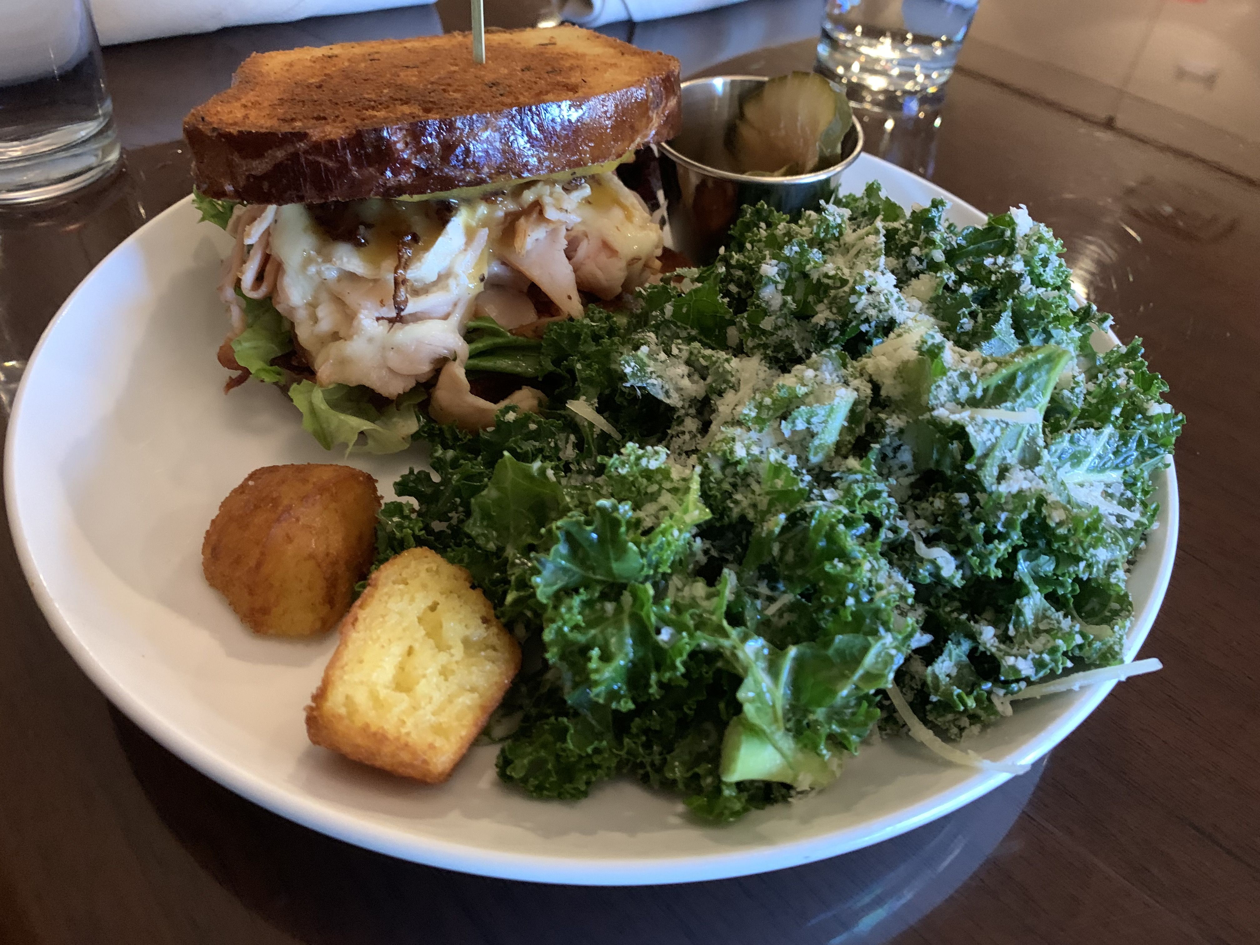 A plate with a sandwich, cornbread bites and salad