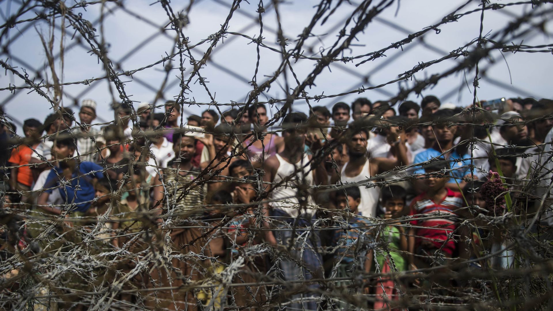 Rohingya refugees standing behind barbed wire.
