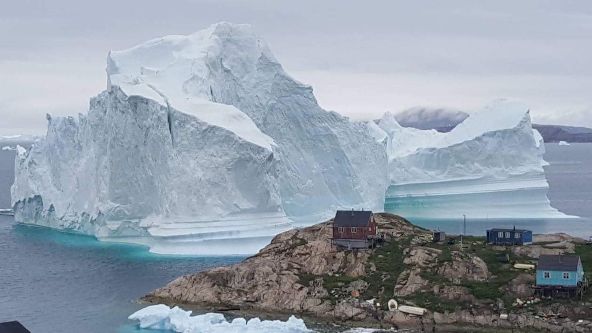 A picture taken on July 13, 2018 shows an iceberg behind houses and buildings after it grounded outside the village of Innaarsuit, Greenland.