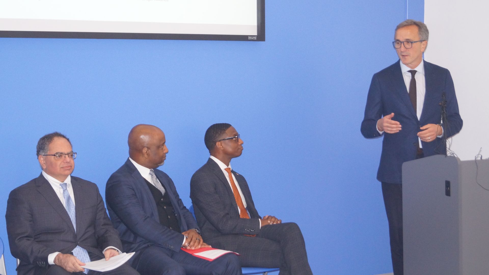 Cleveland Clinic CEO Tom Mihaljevic speaks at a podium, as three men in suits look on. 