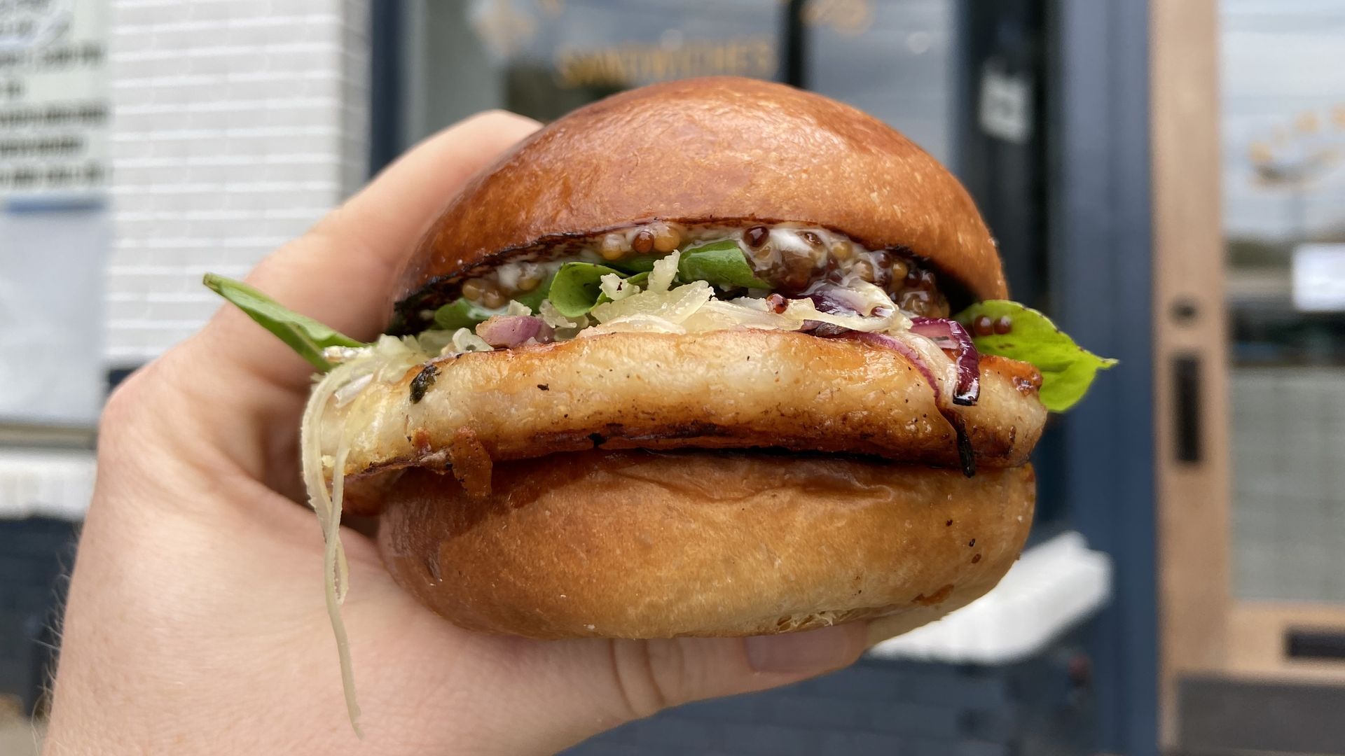 A porchetta sandwich is held in front of the window of Kinship Sundry and Butcher in Atlanta's Virginia-Highland neighborhood