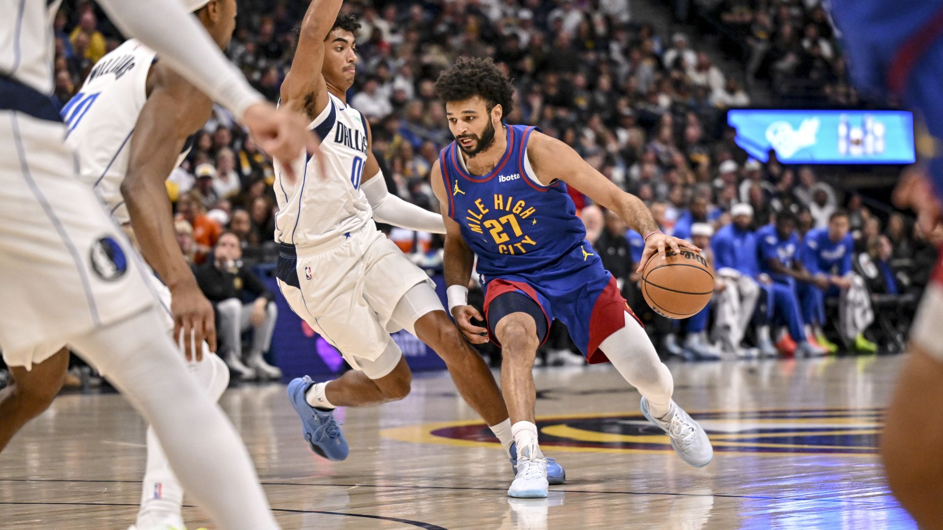 A man in a blue jersey with the words MILE HIGH CITY and 27 in the center holds a basketball while an opposing player stands next to him.