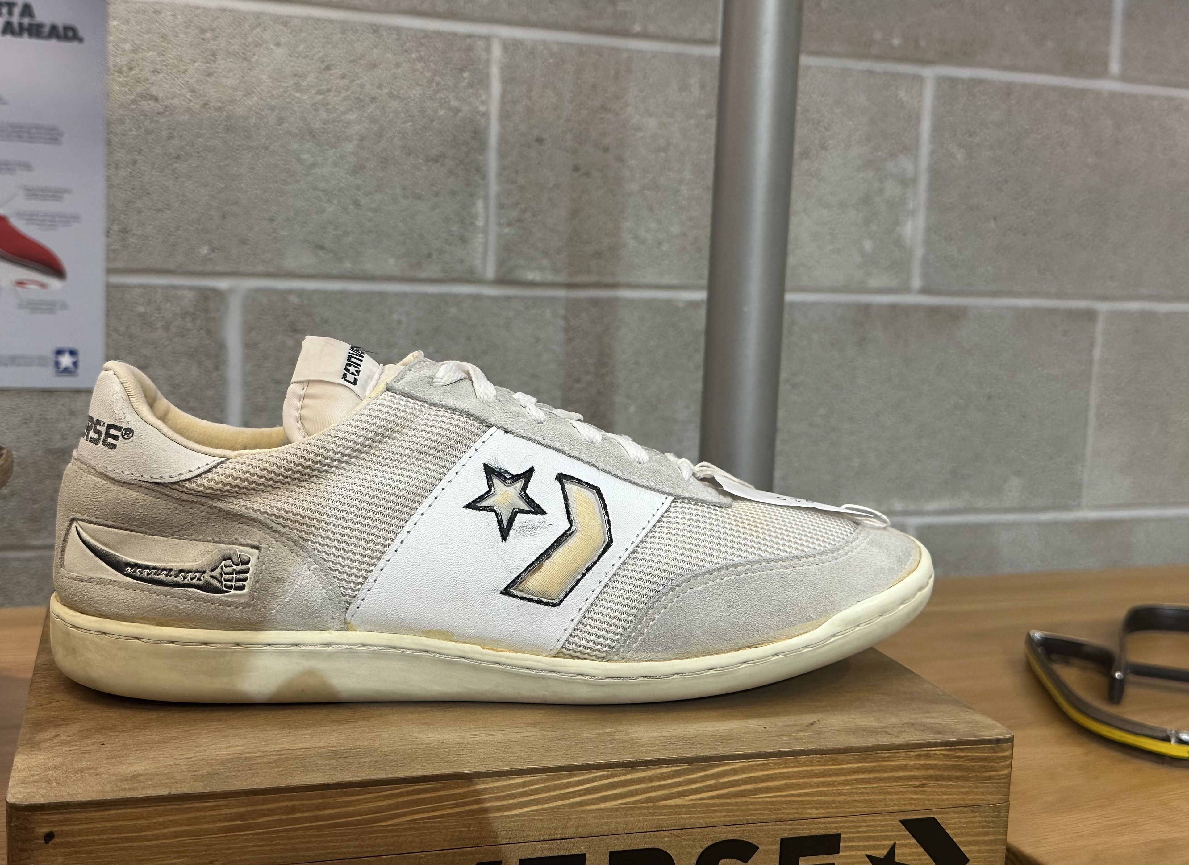 A white Converse sneaker with black details, including a black fist logo that says "martial arts." This was the Converse Street Master sneaker. 