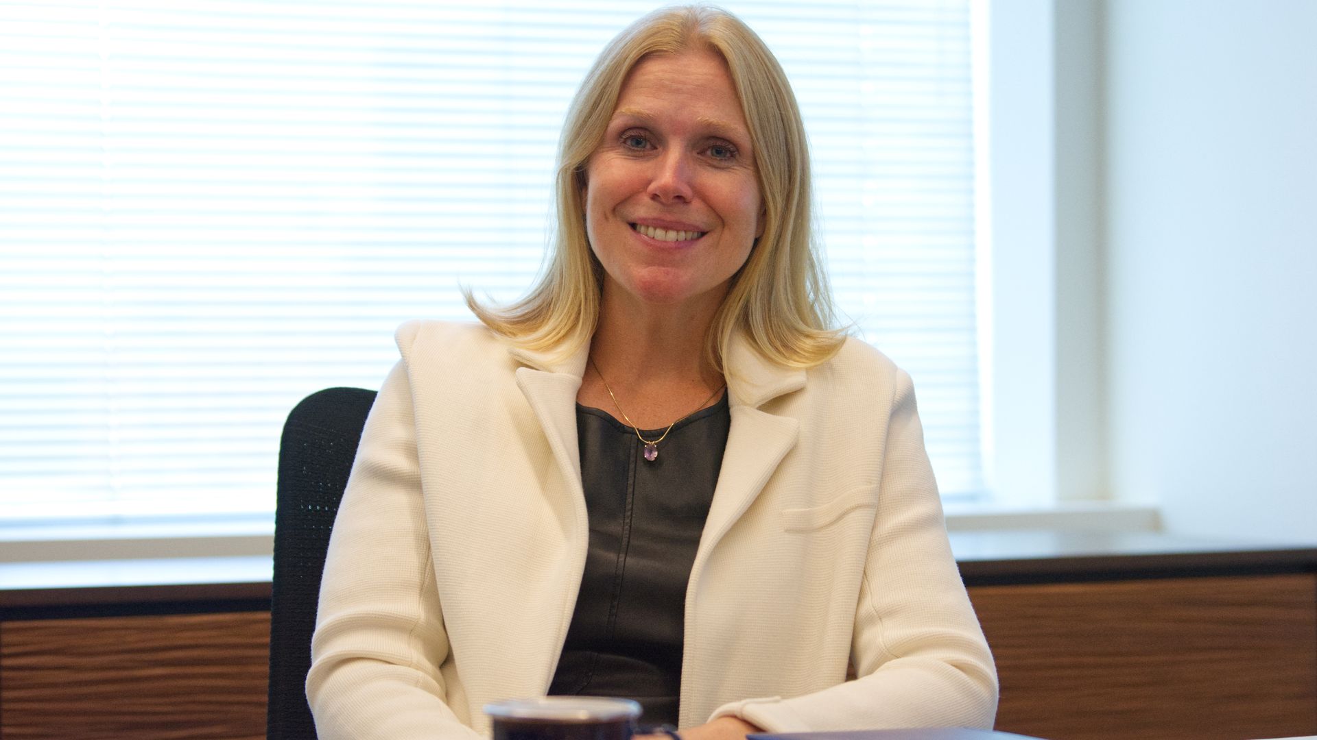 Lauren Knausenberger, a woman with blonde hair, sits at a desk in an office. The blinds behind her are pulled down.