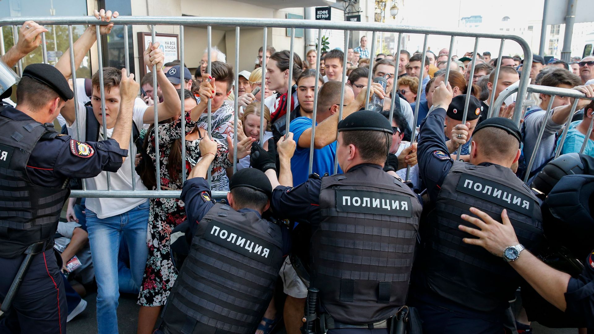 This image shows a line of protestors and police on opposite sides of a steel fence barrier that they are holding against each other.