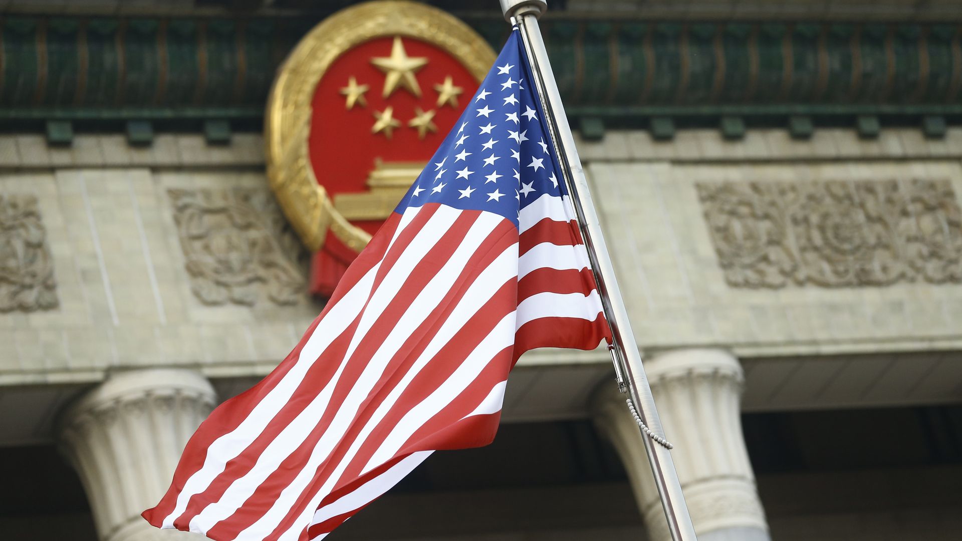 An American flag flies in front of a Chinese emblem. 