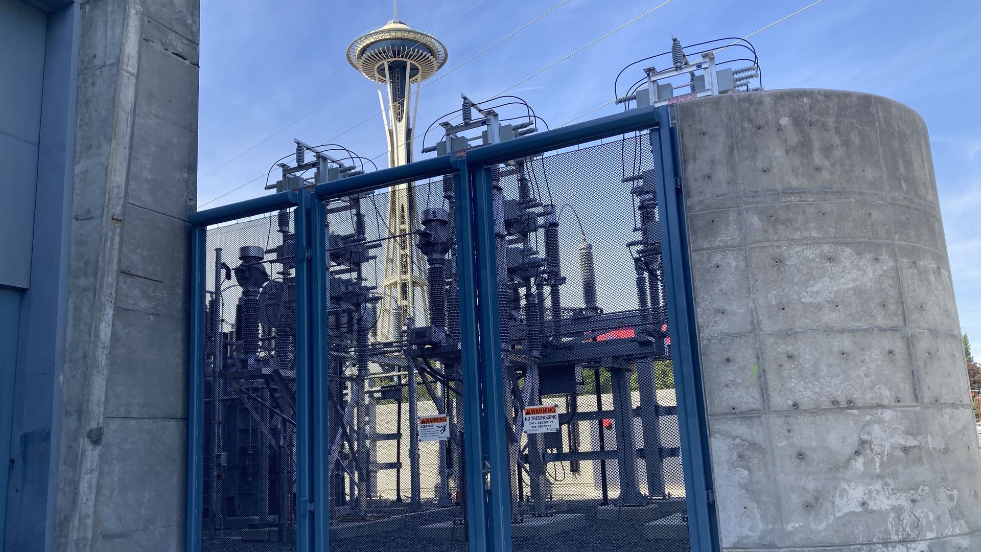 A concrete structure with a blue fence-like door is shown with the Space Needle in the background.