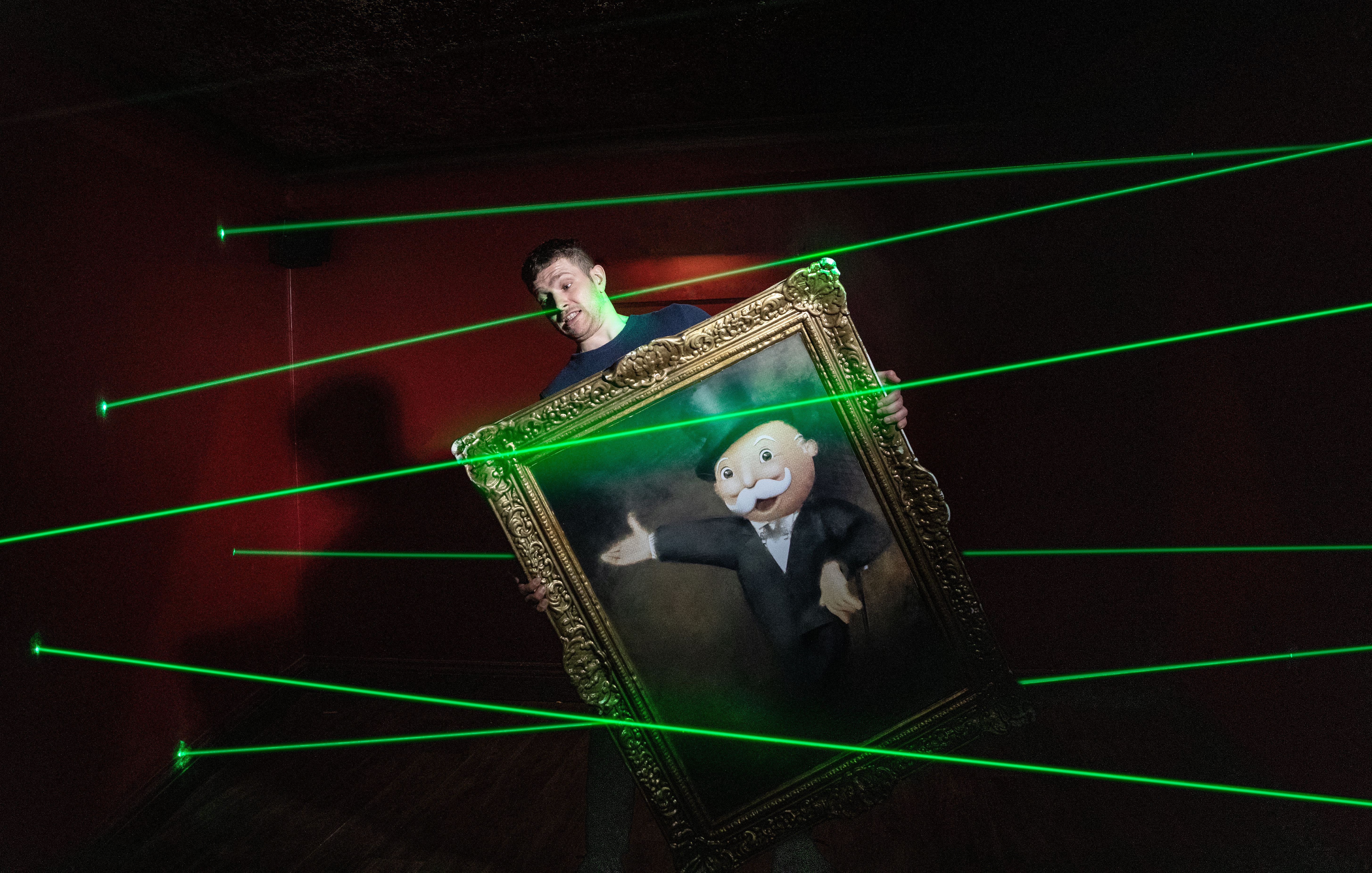 People holds a portrait of Monopoly man in room with green lasers