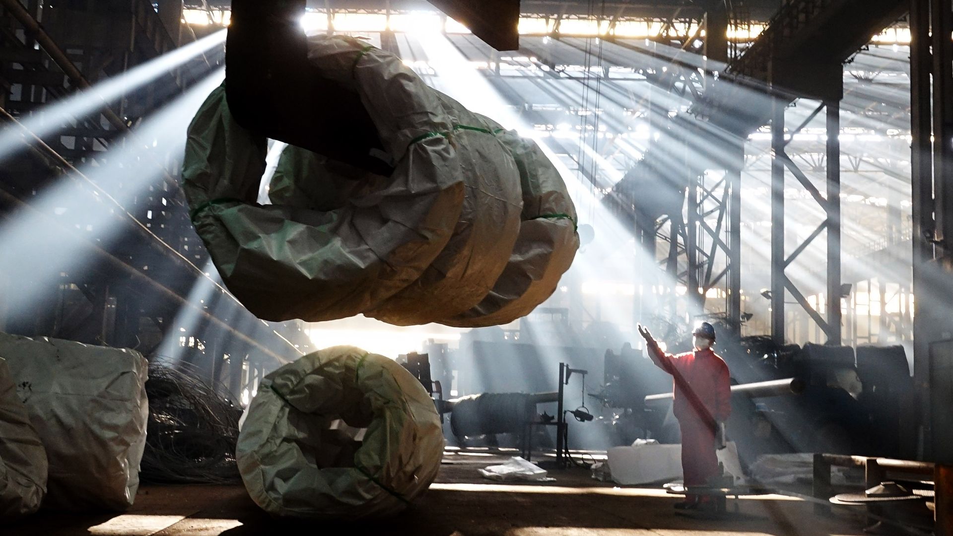 worker on factory floor below suspended steel coil
