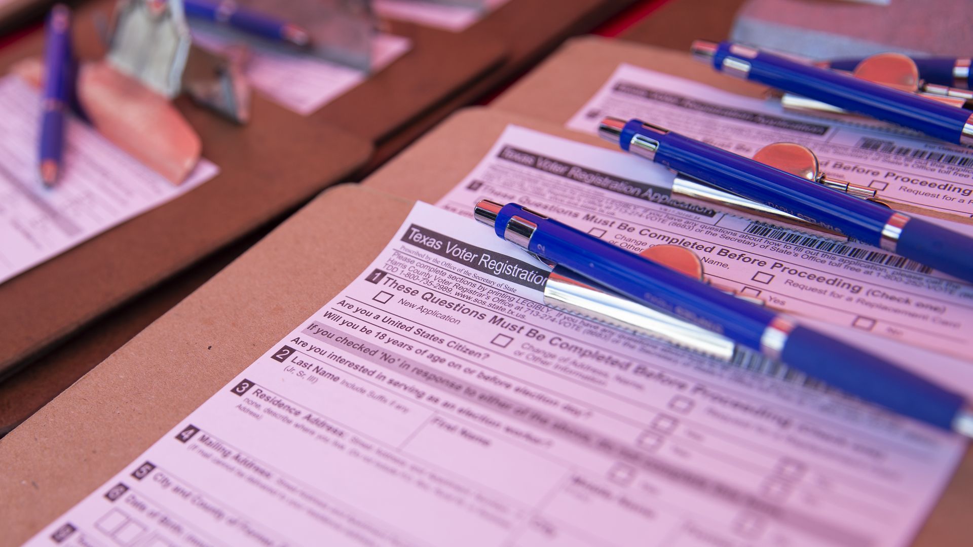 A stack of Texas voter registration forms on clipboards with blue pens.