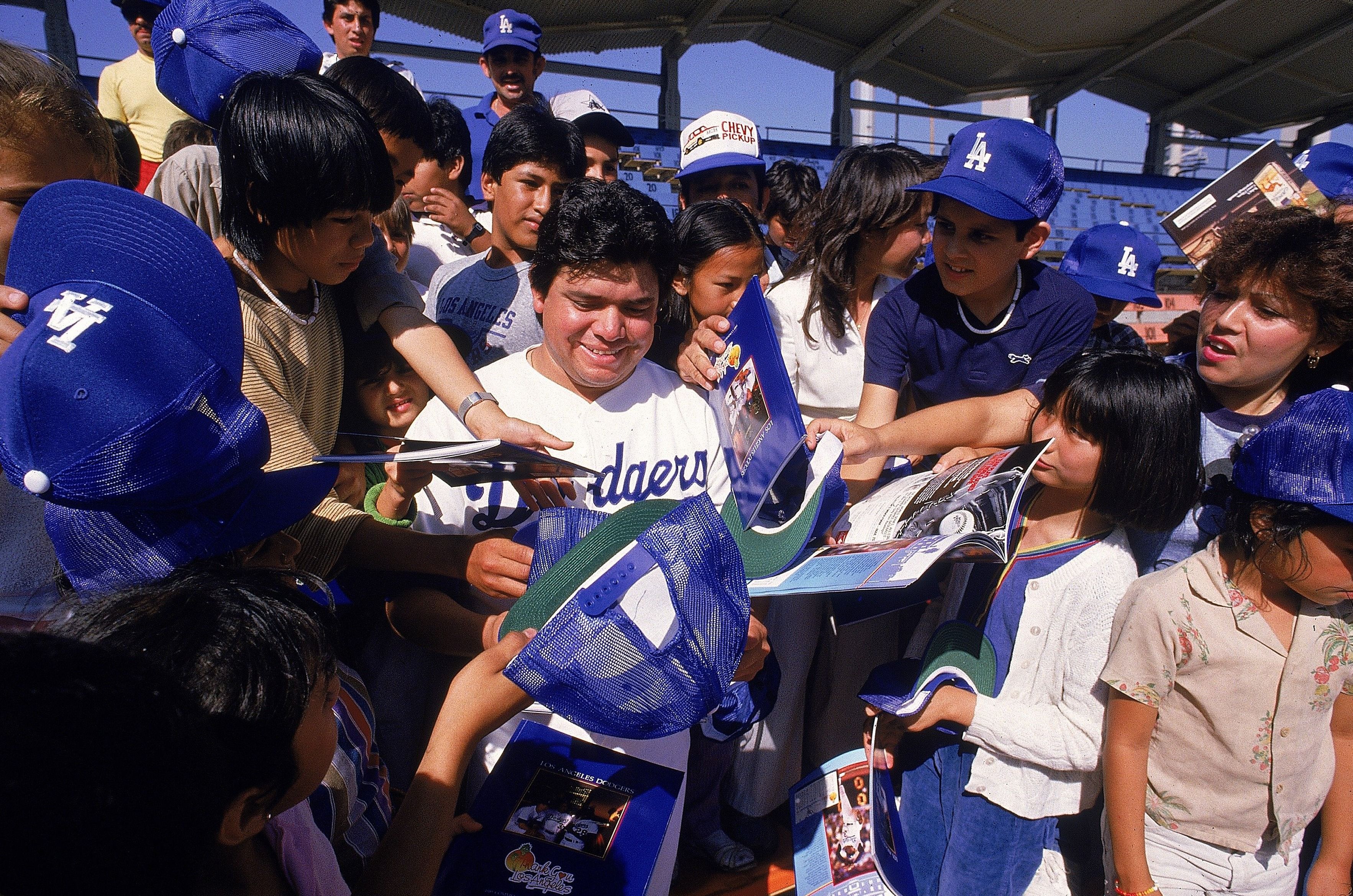 Fernando Valenzuela signs autographs while surrounded by children.