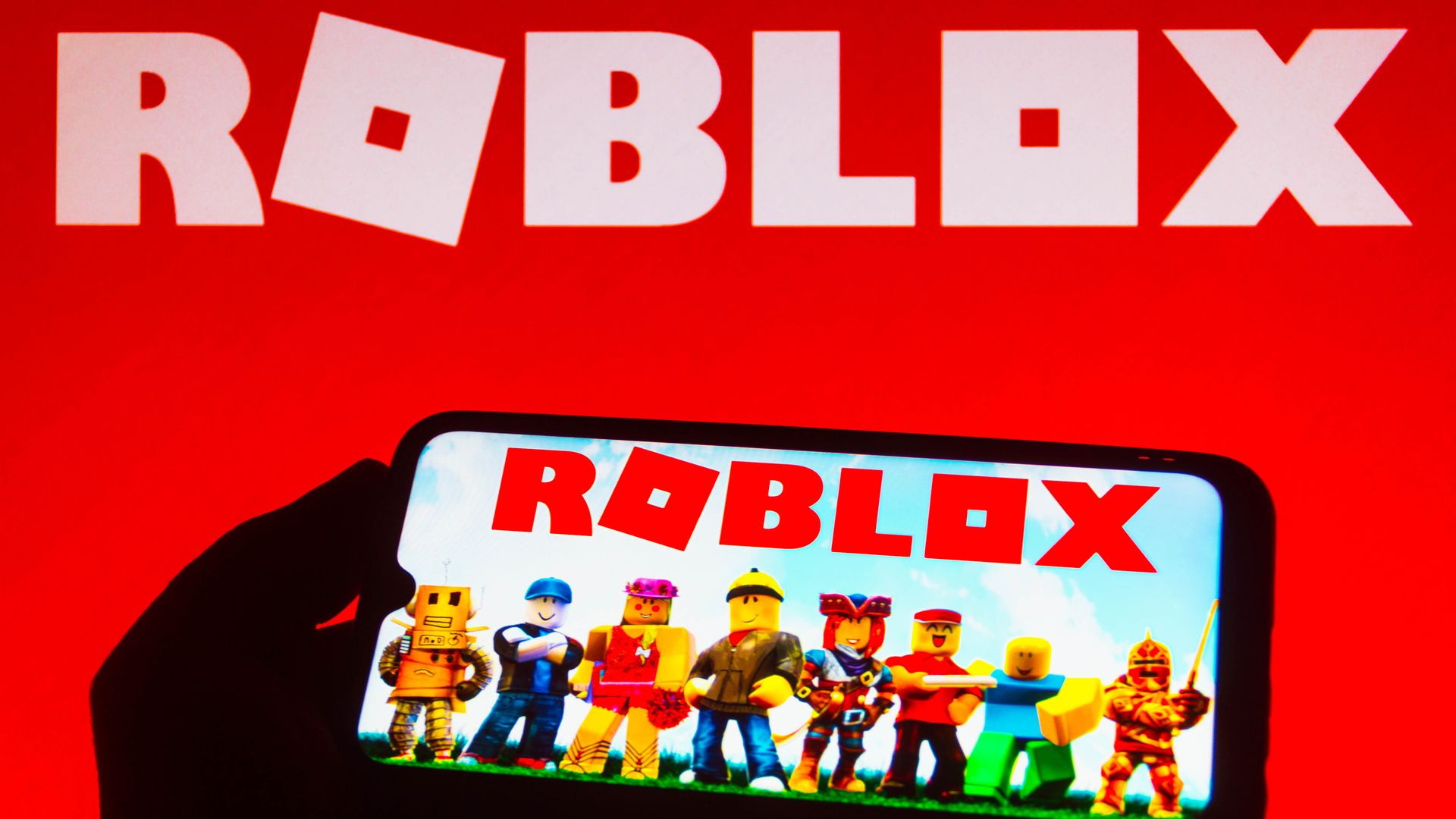 The Roblox logo with a phone having the app open