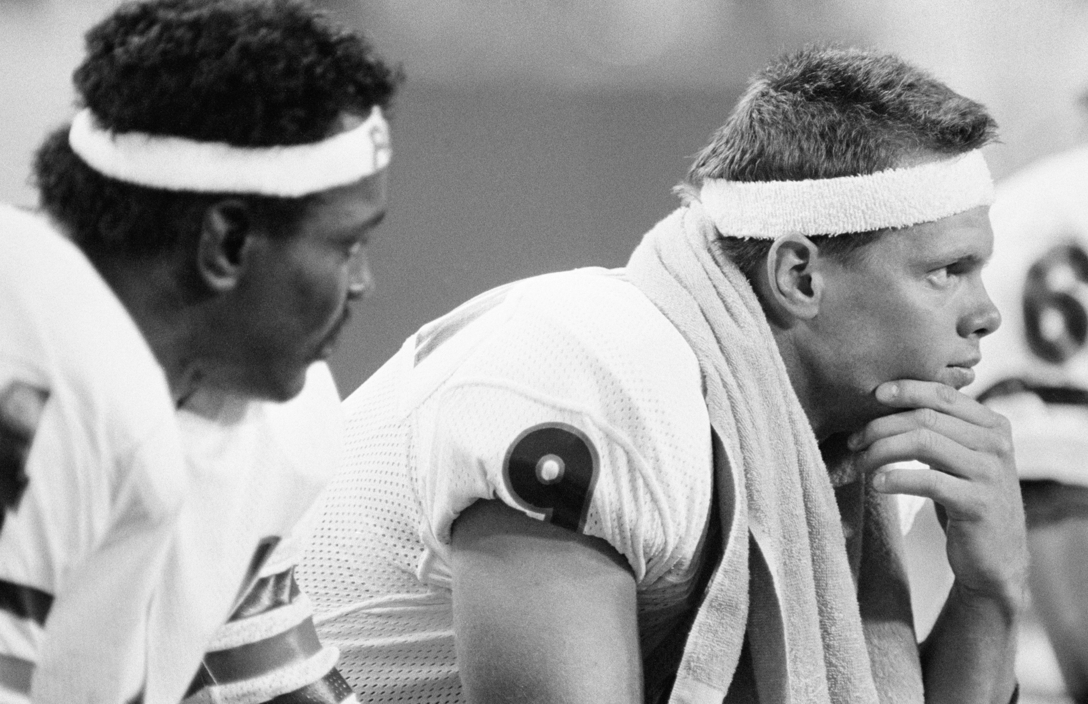 Photo of two football players in uniform sitting on the bench. 