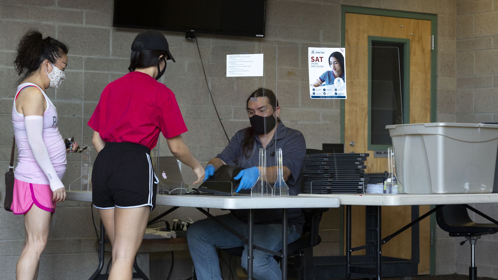 An employee wearing a protective mask distributes laptop computers to students at Catalina Foothills High School in Tucson, Arizona, U.S., on Friday, Aug. 14, 2020.