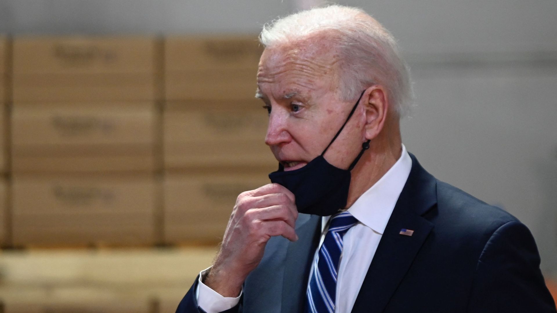 Biden wears a face mask and a suit while talking