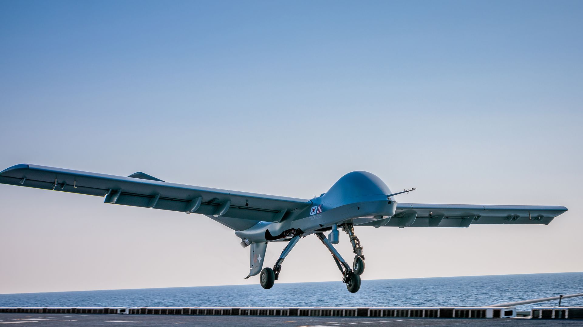 A Gray Eagle drone with American and South Korean markings lands on an aircraft carrier.