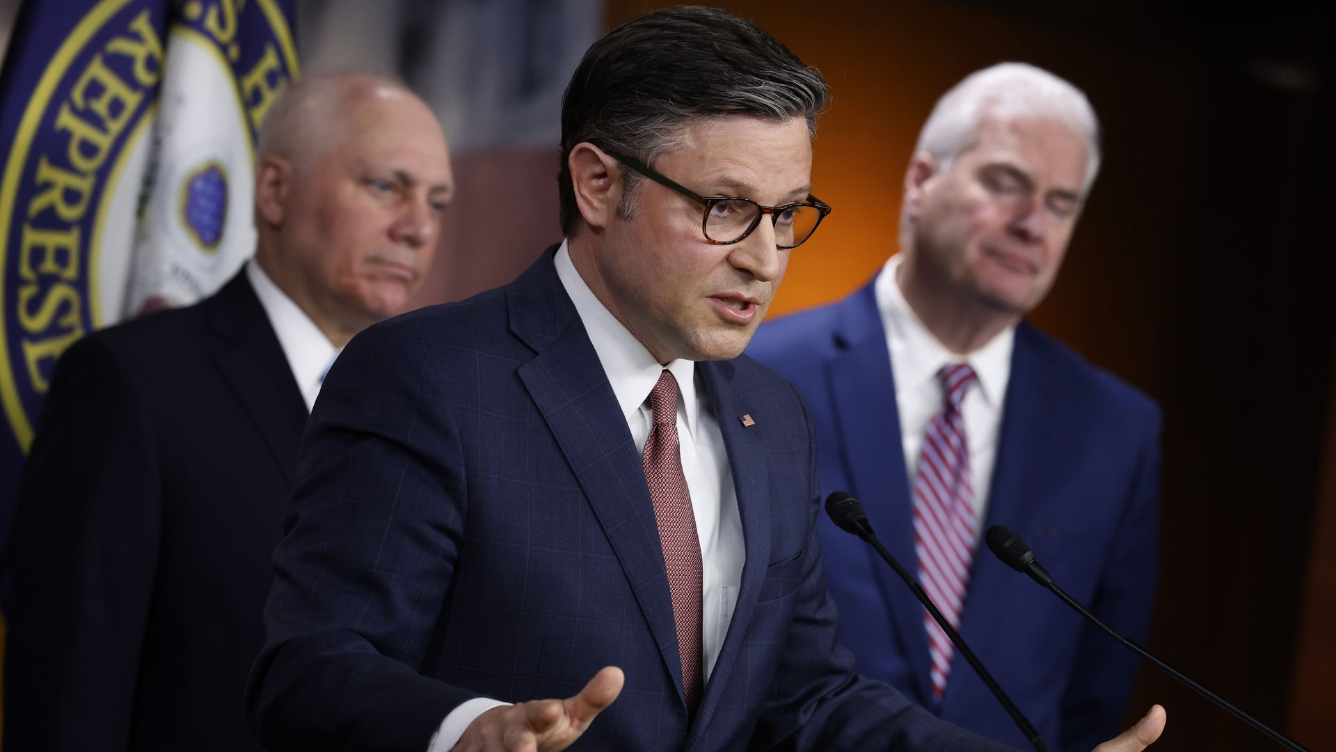 House Speaker Mike Johnson, wearing a dark blue suit, white shirt and red tie, flanked by Majority Leader Steve Scalise and Whip Tom Emmer.