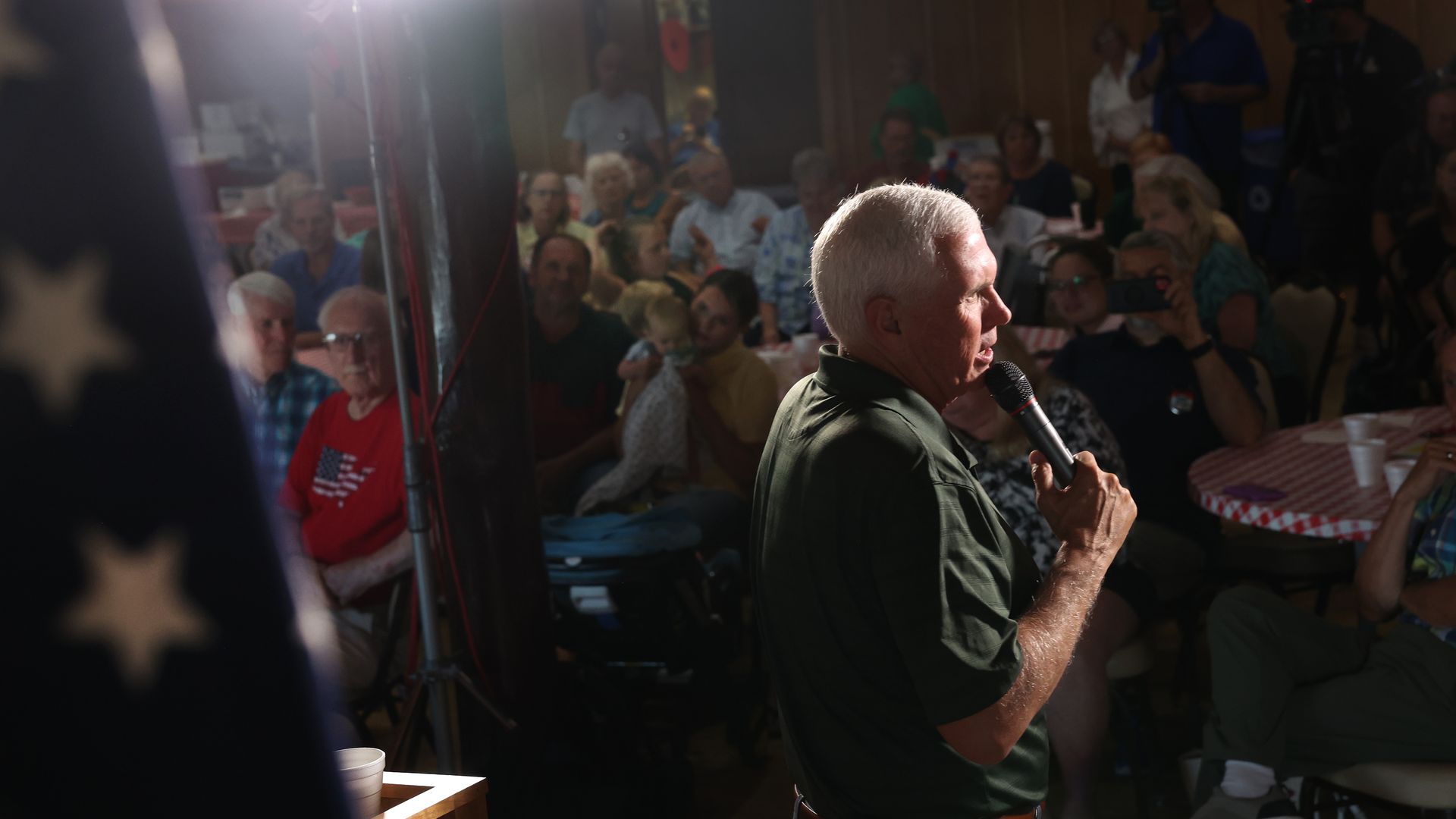 Mike Pence wanders a room, holding a microphone and talking to an audience at the Clinton County GOP Hog Roast in Clinton, Iowa.