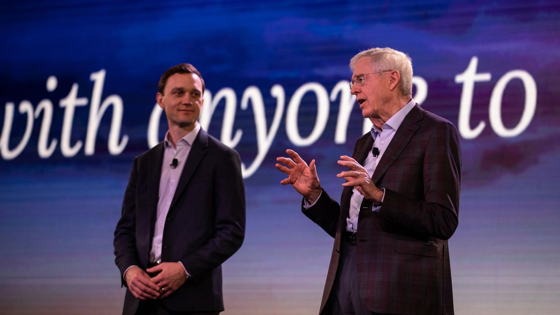 Two men stand next to each other while one of them speaks