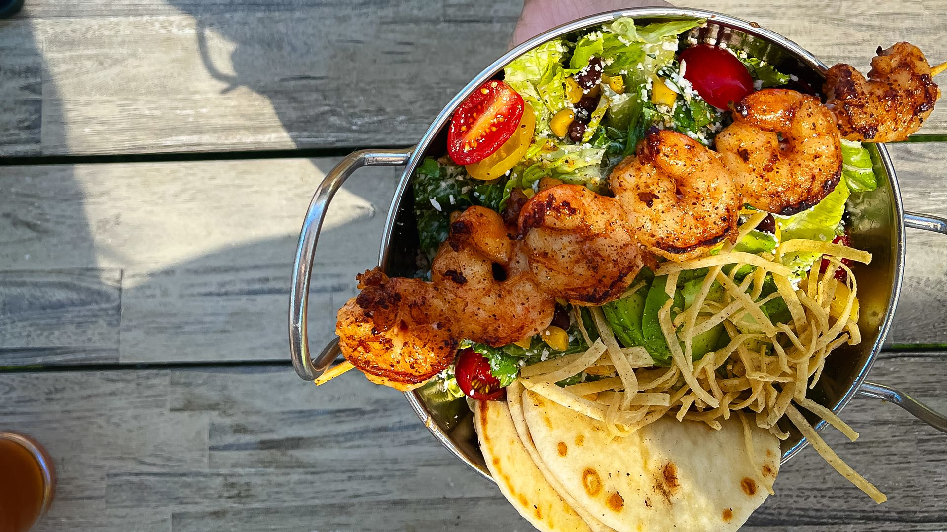 A salad in a bowl with a skewer of shrimp across it. 