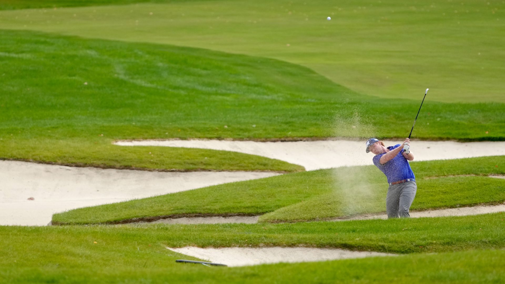A golfer hits a shot out of the sandy bunker. 