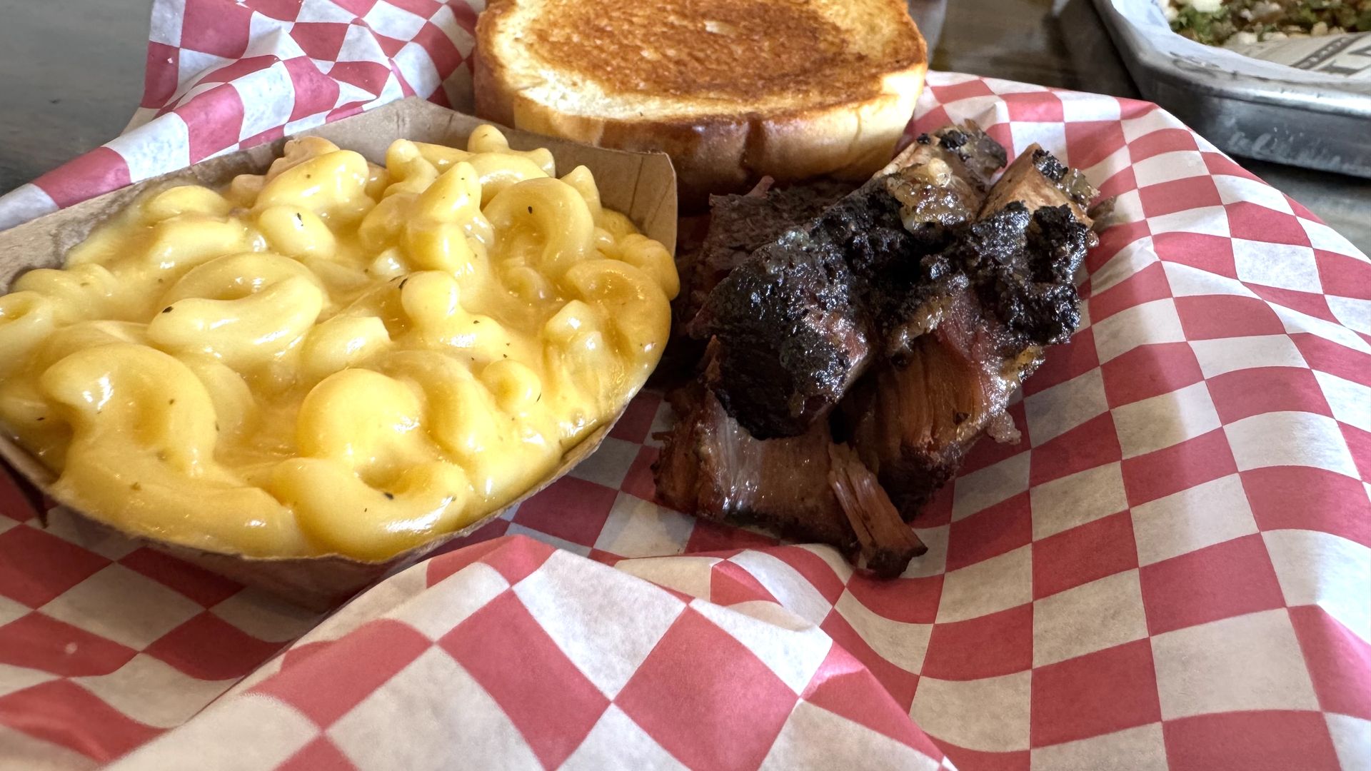 A plate of food showing a boat of mac and cheese, a pile of brisket and a piece of Texas toast.