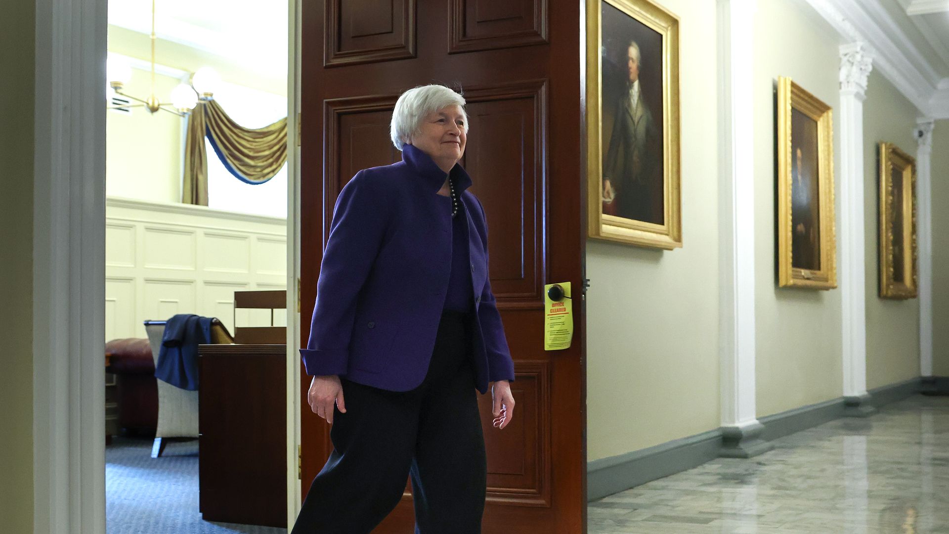 Janet Yellen walks out of a door in a purple suit to meeting some people we don't see but presumer are there