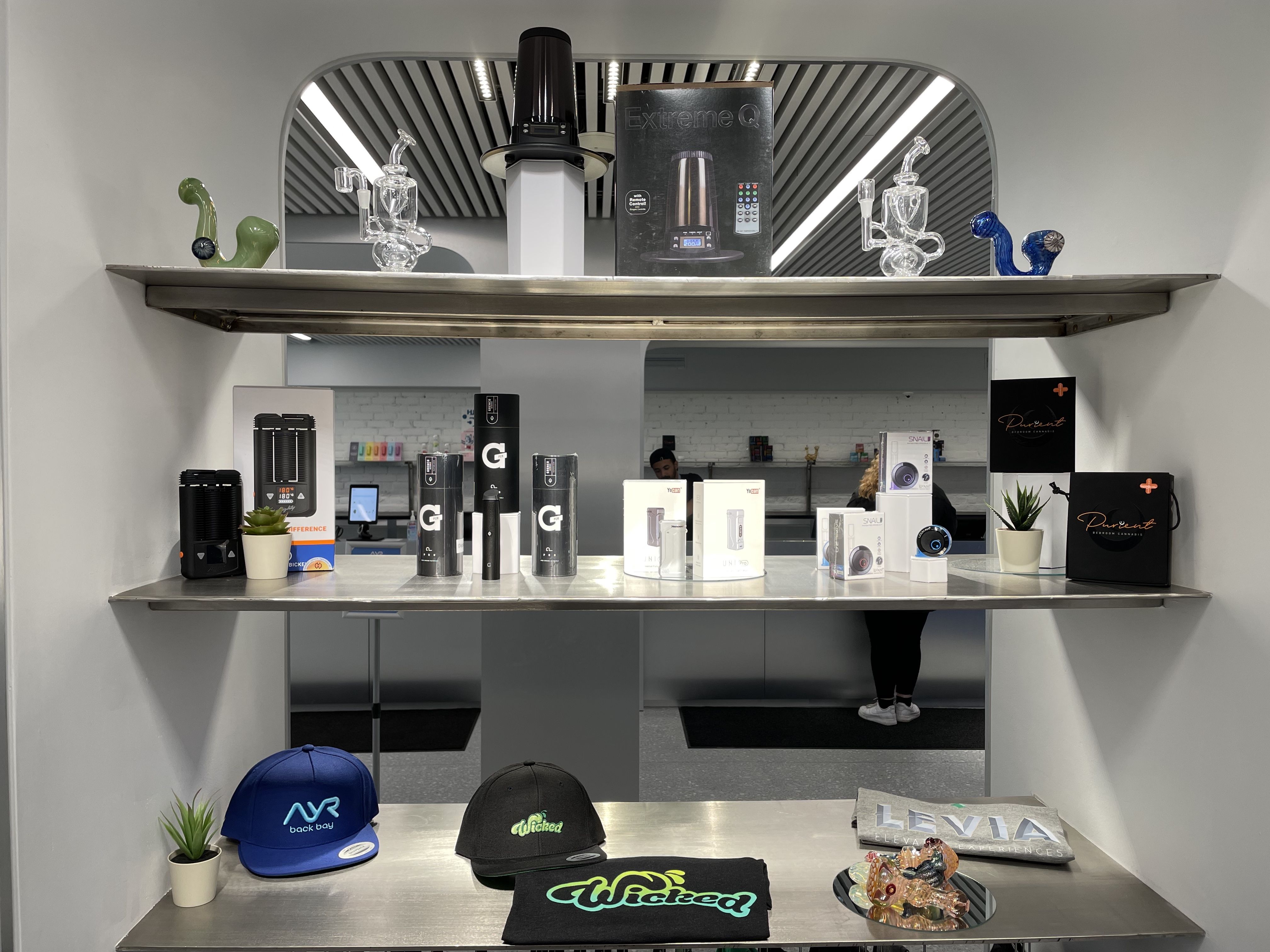Three product shelves include baseball caps, a black T-shirt, a multicolored cannabis bowl and other products.
