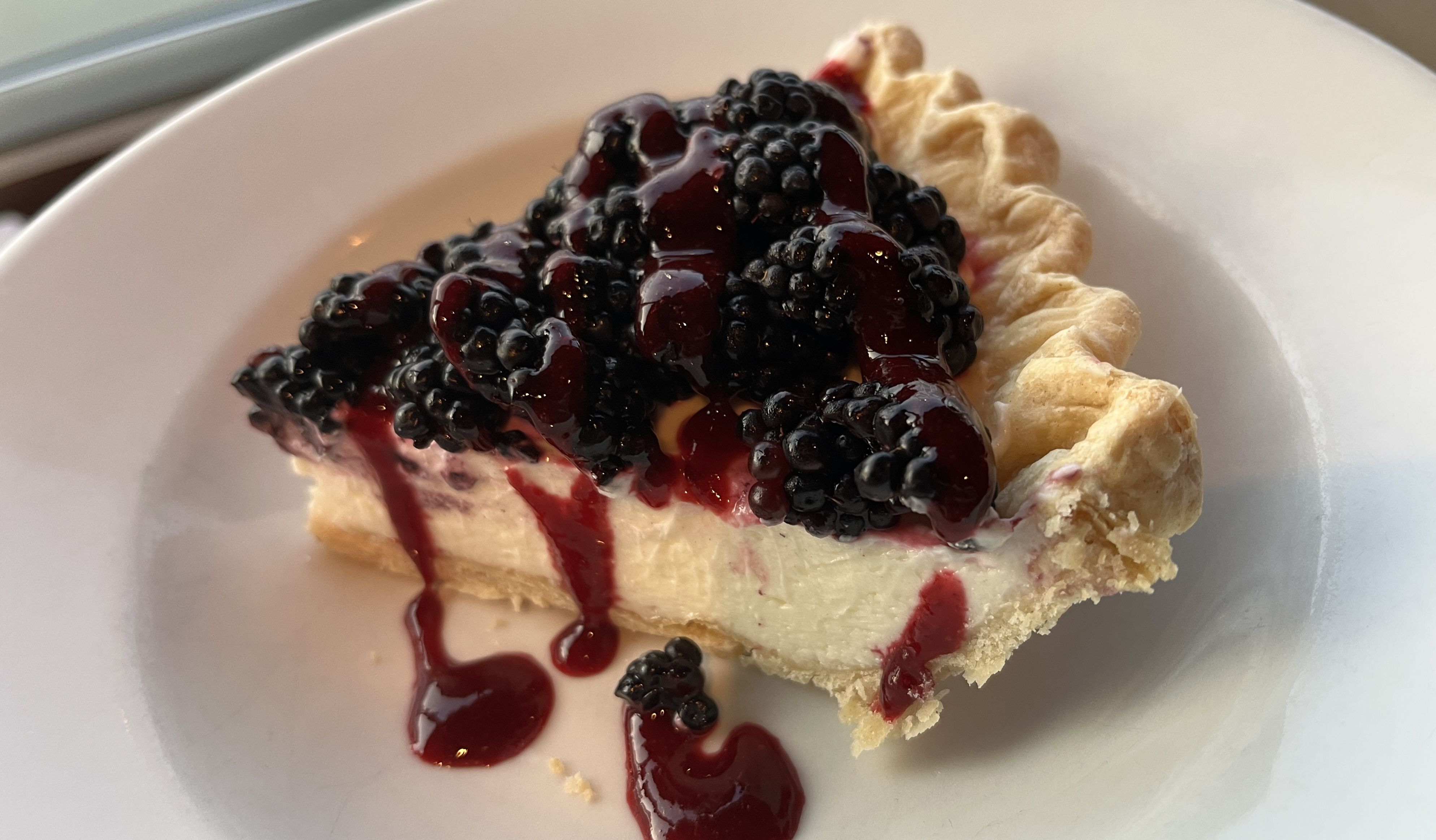 Slice of creamy cheesecake topped with fresh blackberries and dark red berry sauce on a white plate.