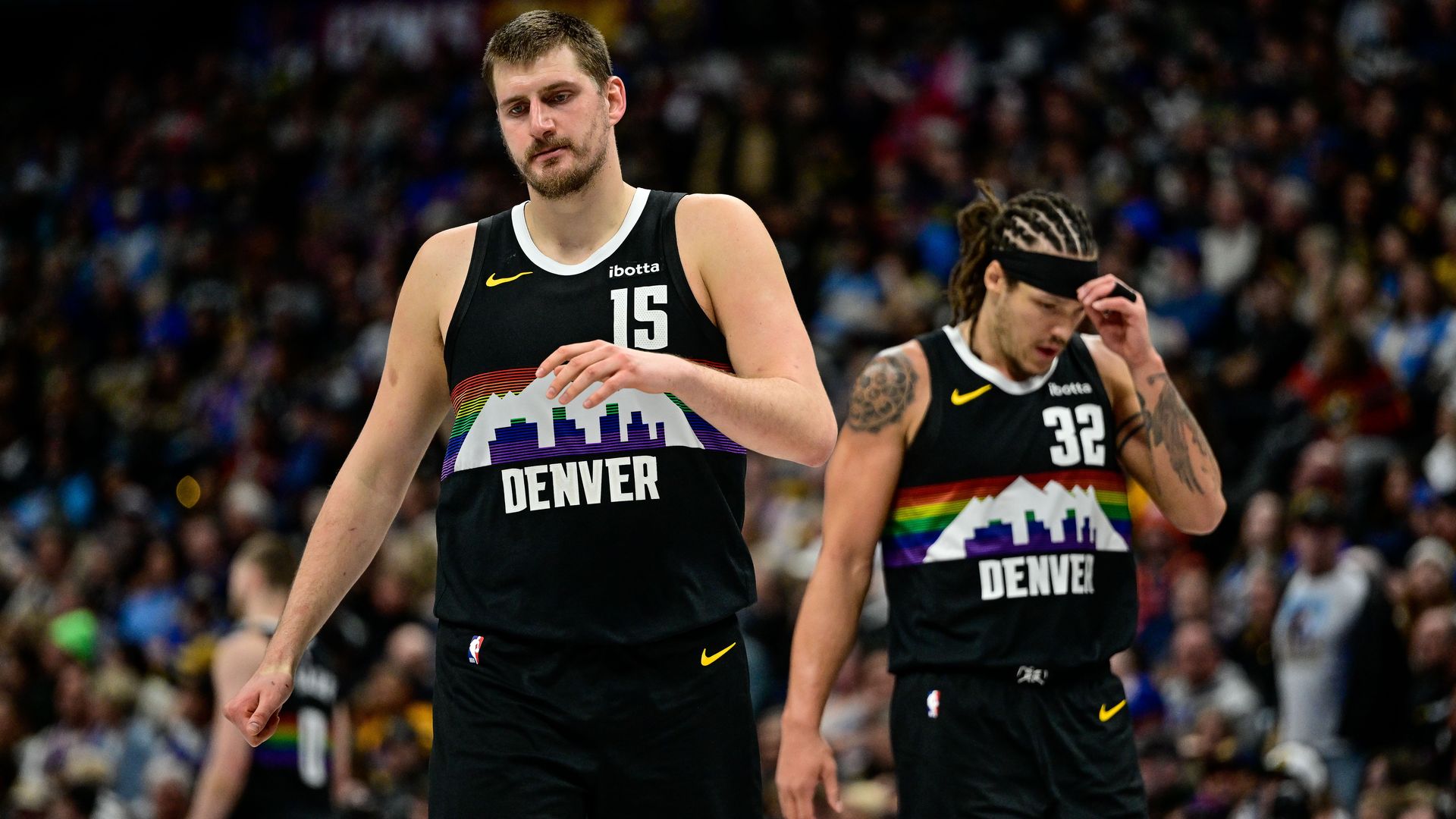 Two Denver Nuggets players in black rainbow-themed jerseys with DENVER and a city skyline. Number 15 in front, number 32 behind, crowd in the stands.