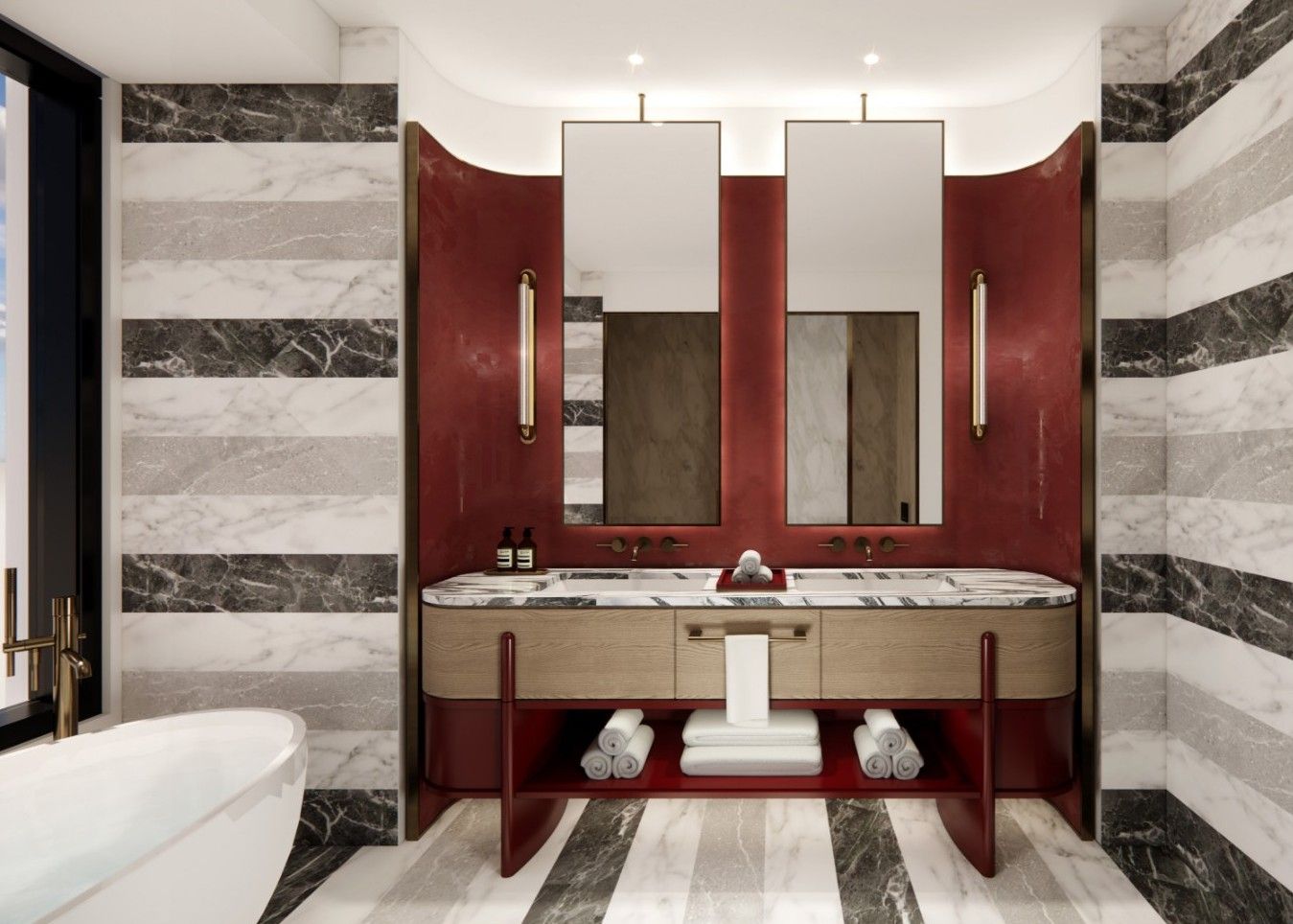 Lux bathroom with a red curved vanity featuring a marble countertop, two mirrors, and gold sconces; striped marble walls, towels under the sink, and a white freestanding tub to the left.