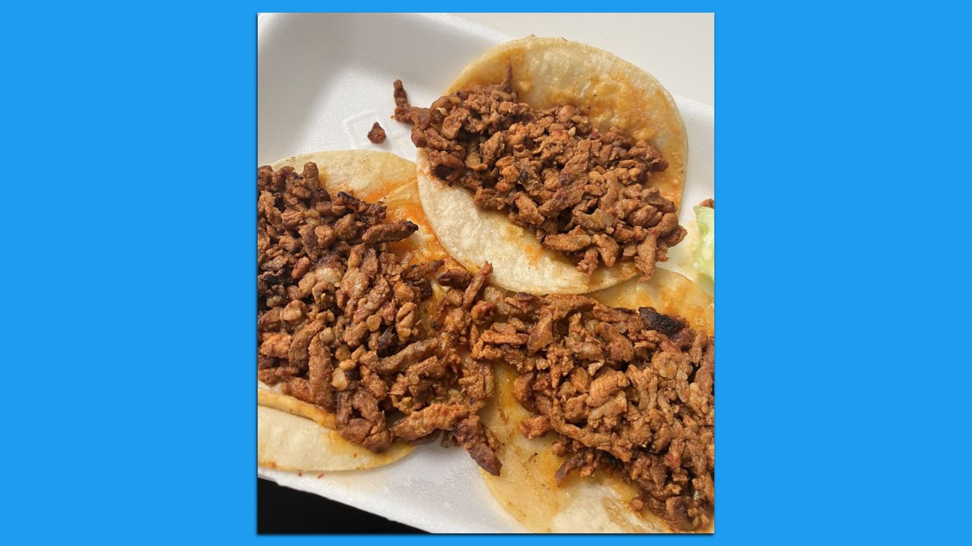 Three soft tacos filled with seasoned cooked ground meat on a white foam tray, with a small portion of shredded lettuce visible on the side.